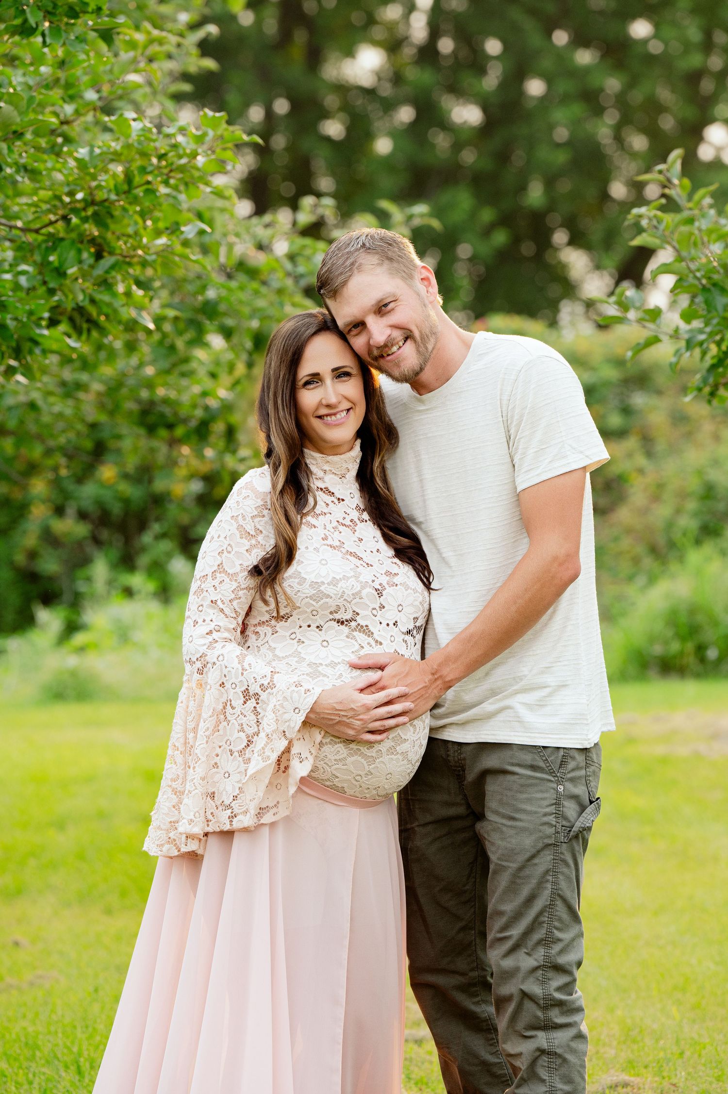 Couple embracing during outdoor maternity photo session in garden.