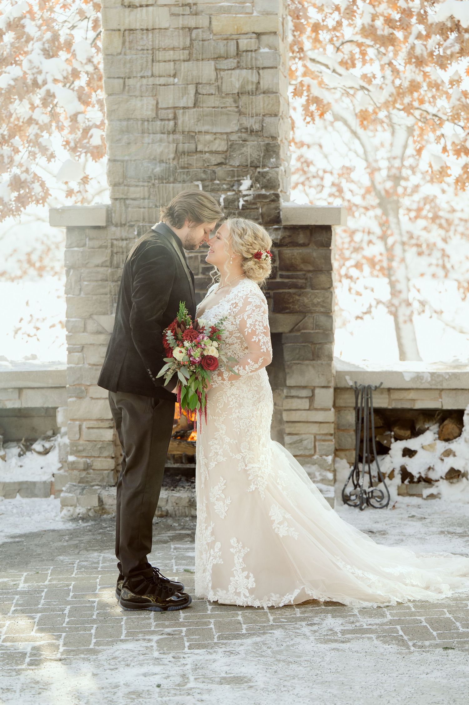 Romantic winter wedding couple shares intimate moments against stone wall backdrop in snowy setting.