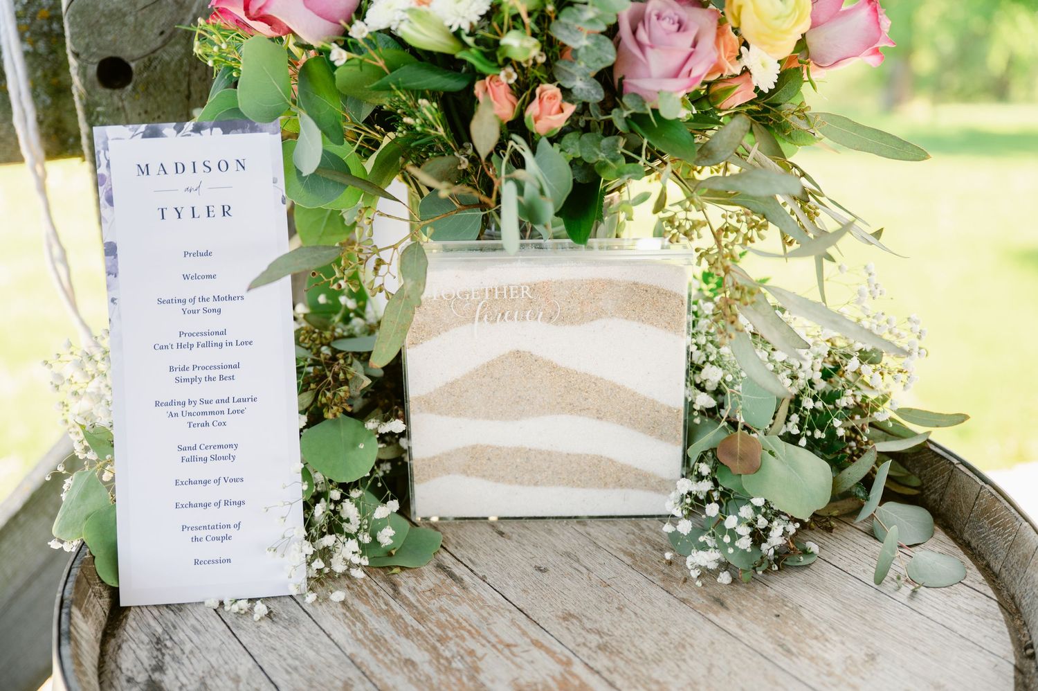 Wedding menu and floral arrangement with pink roses displayed on rustic wooden surface.