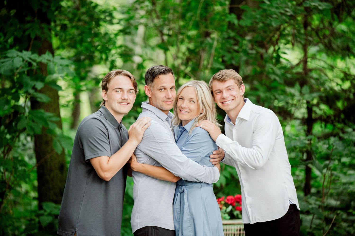 Clear Lake MN Family PhoA group of four people in casual attire pose together outdoors against a green leafy background in natural lighting.