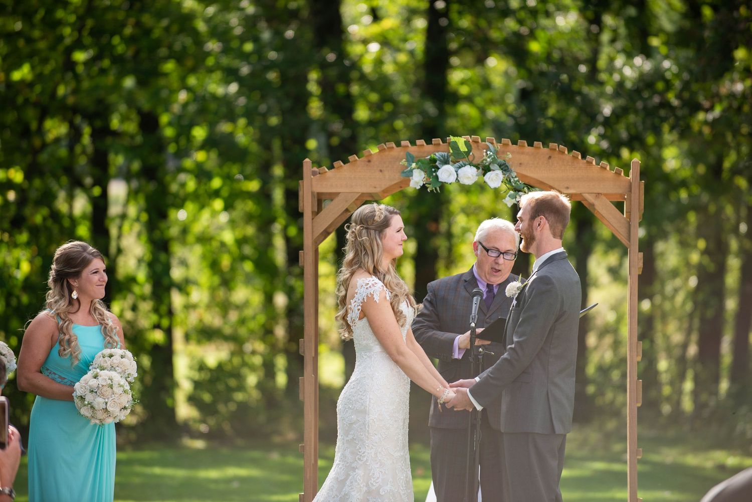 An outdoor wedding ceremony takes place under a wooden arch with turquoise accents. Rum River Barn Milaca Minnesota Weddings