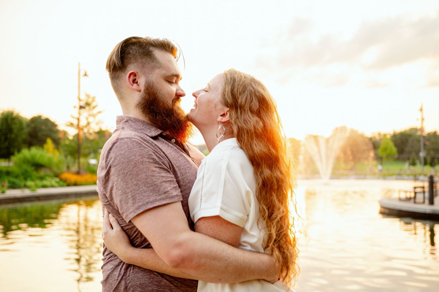 Couple sharing a tender moment at sunset by the waterfront with golden light reflecting on the water.