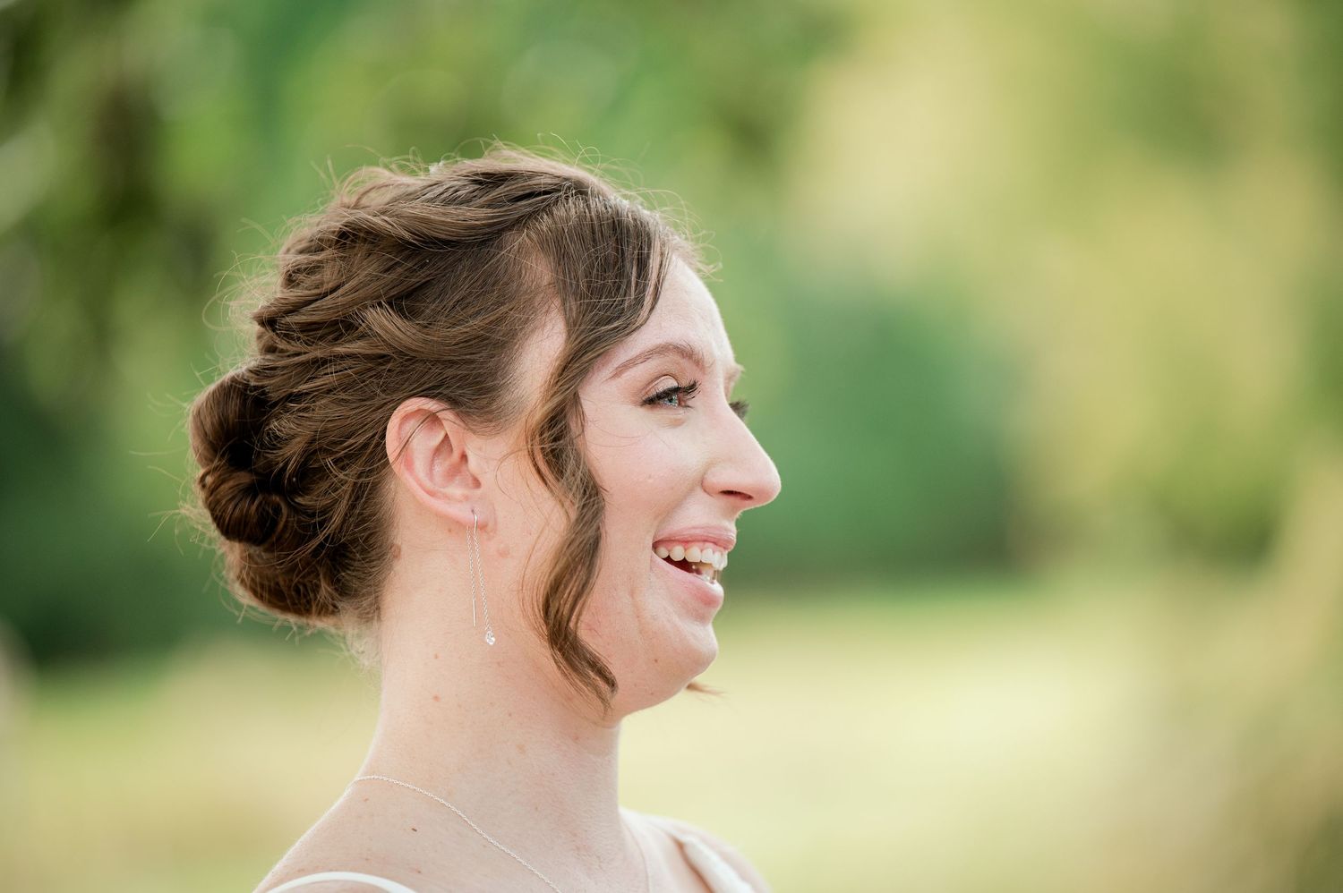 A couple exchanges joyful smiles during their outdoor wedding ceremony beneath natural greenery.