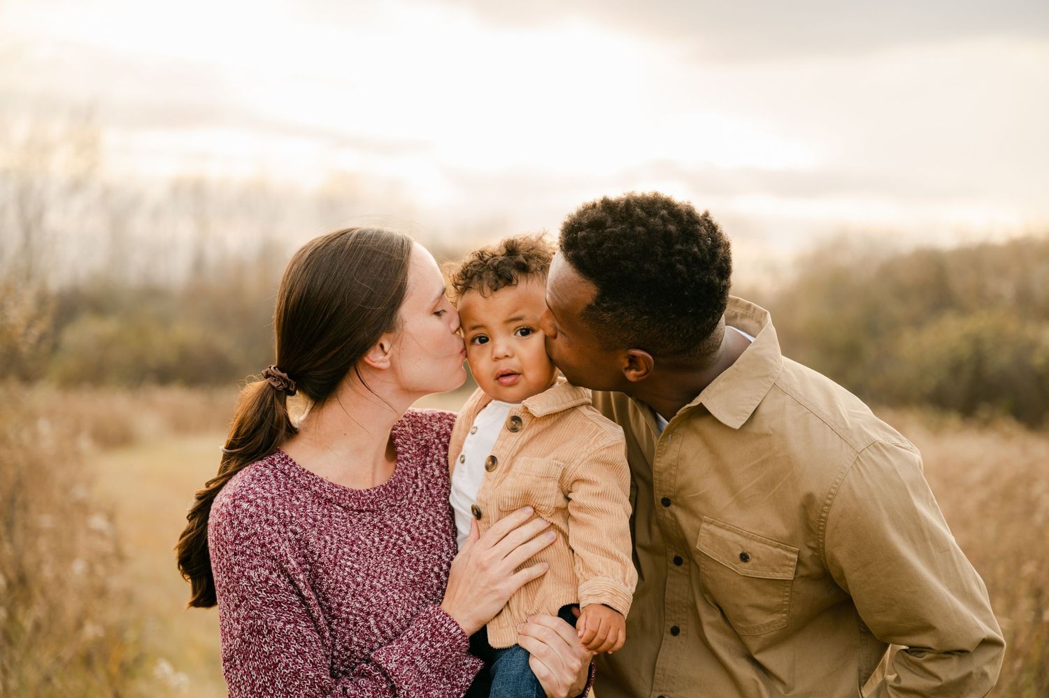 Parents share a tender moment with their young child in an autumn field at sunset. Princeton MN Milestone, Maternity and Newborn P