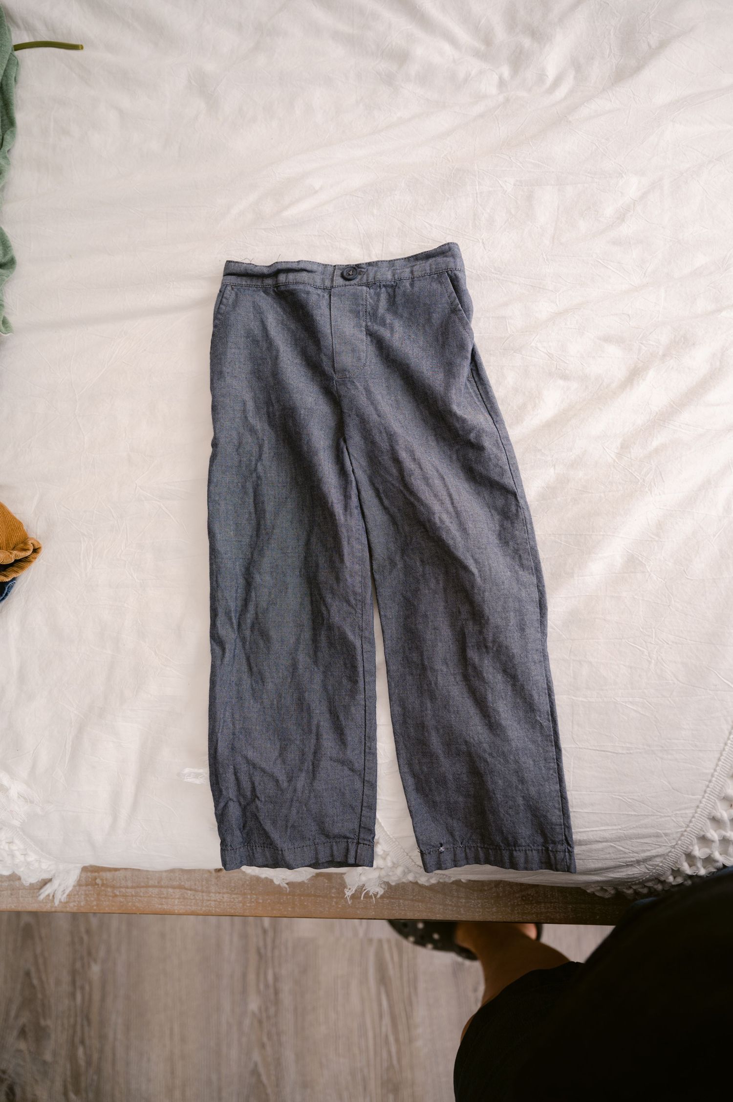 A pair of casual grey linen pants laid flat on a white surface showing their relaxed, loose-fitting silhouette.