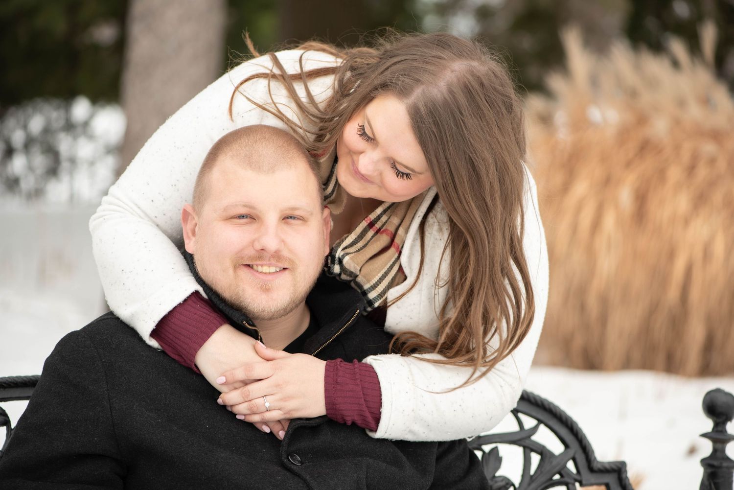 A couple embraces outdoors in winter, with the person in white hugging from behind while seated on a wheelchair.