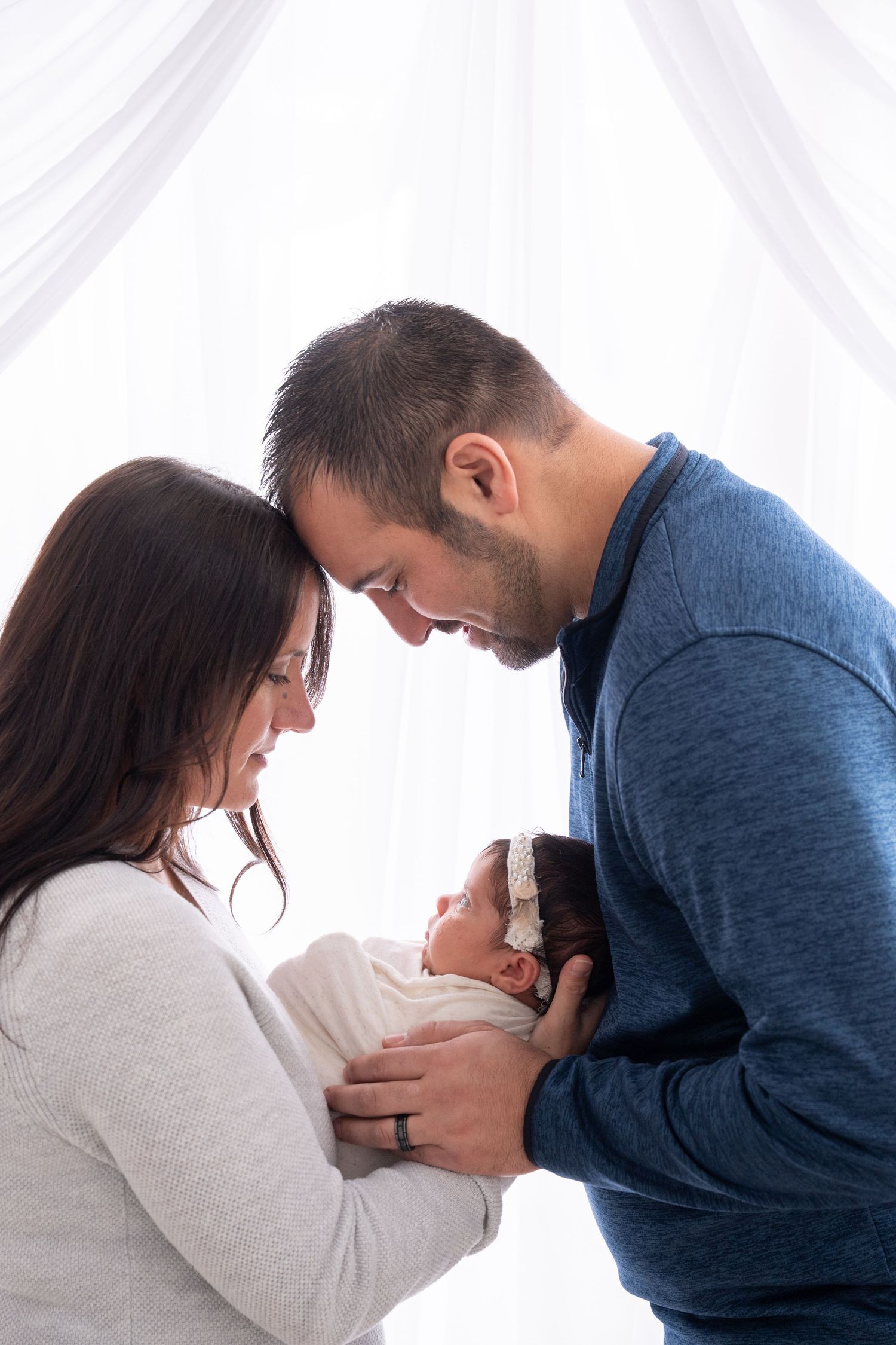 Intimate family moment with parents leaning in close to their newborn.