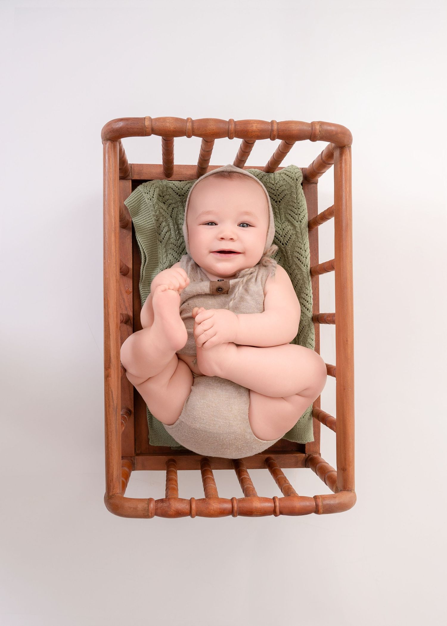 Baby resting in wooden basket with green cushioning against white background.