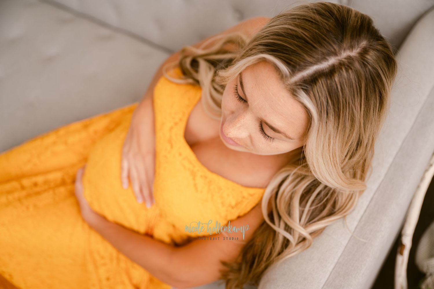 Overhead view of woman in bright yellow dress reclining comfortably on beige couch.