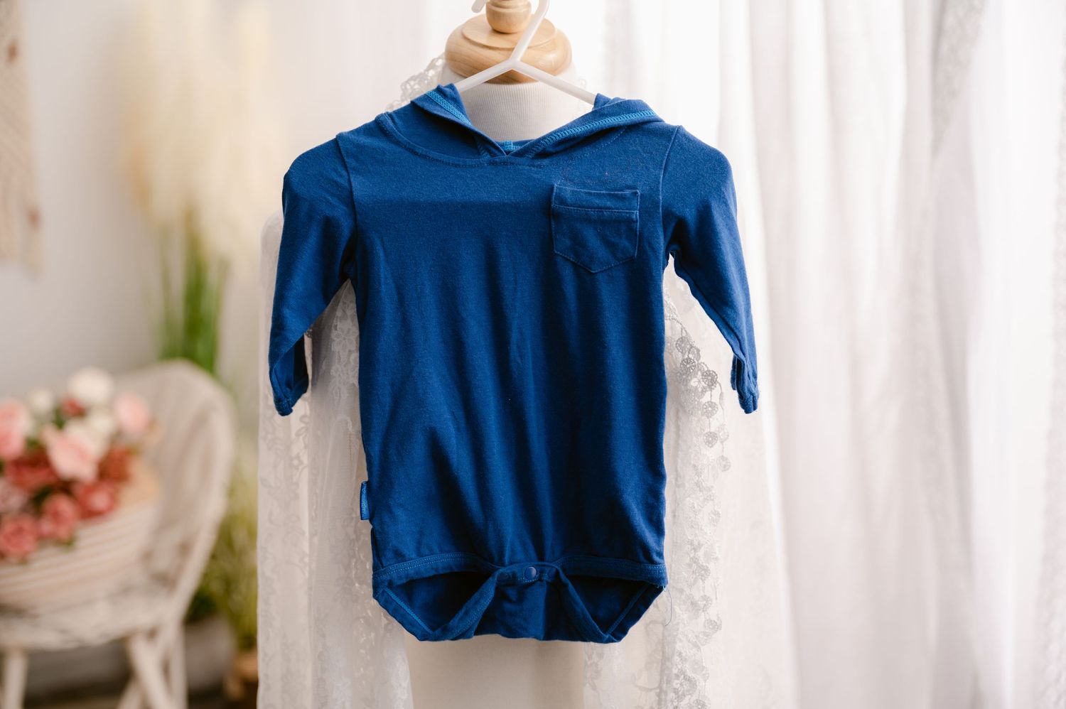 Navy blue hooded infant romper or bodysuit hanging against a light curtain background.