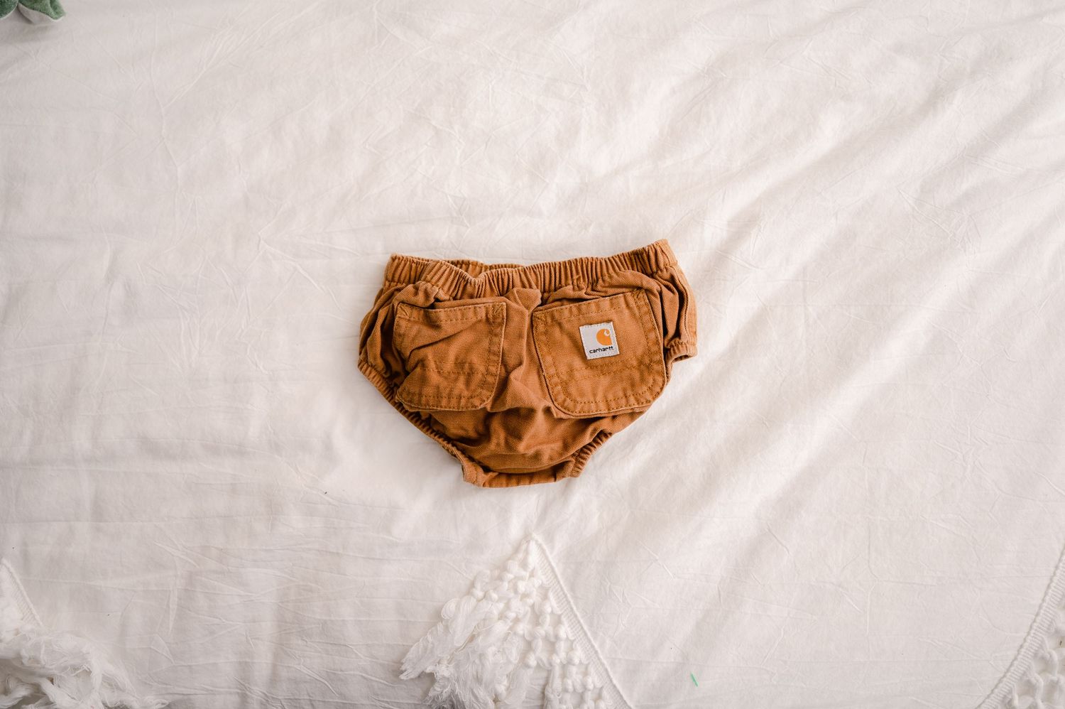 Brown corduroy baby diaper cover with utility pockets lies on white fabric background.