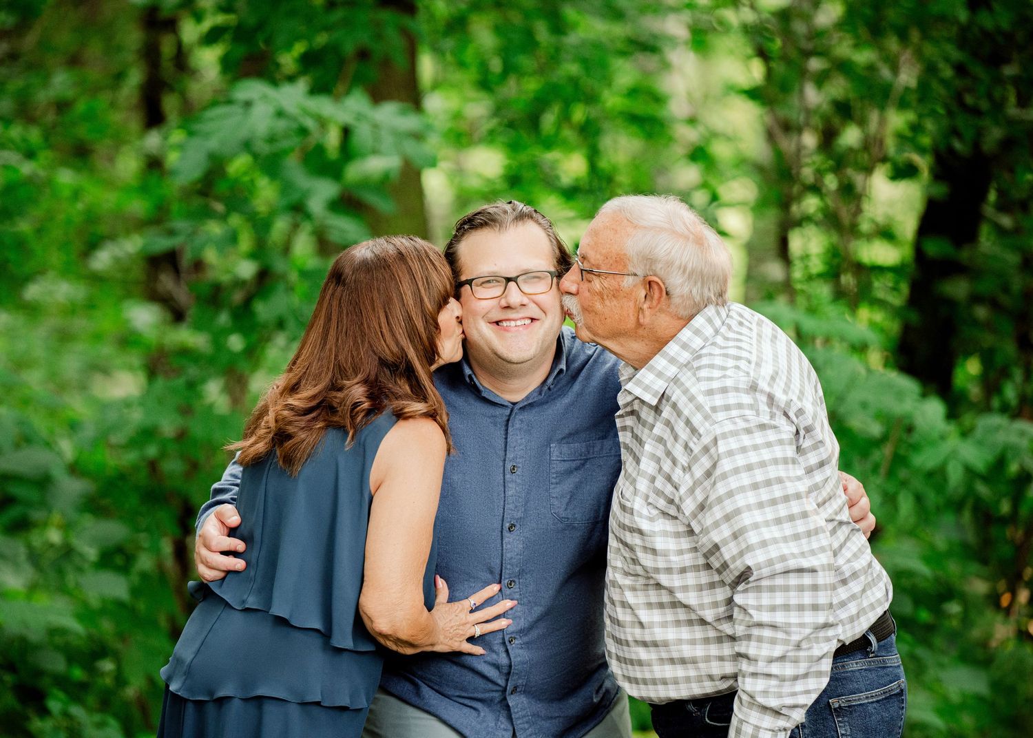 Clear Lake Family Photography: Three people embrace outdoors against a green leafy background in a touching family moment.