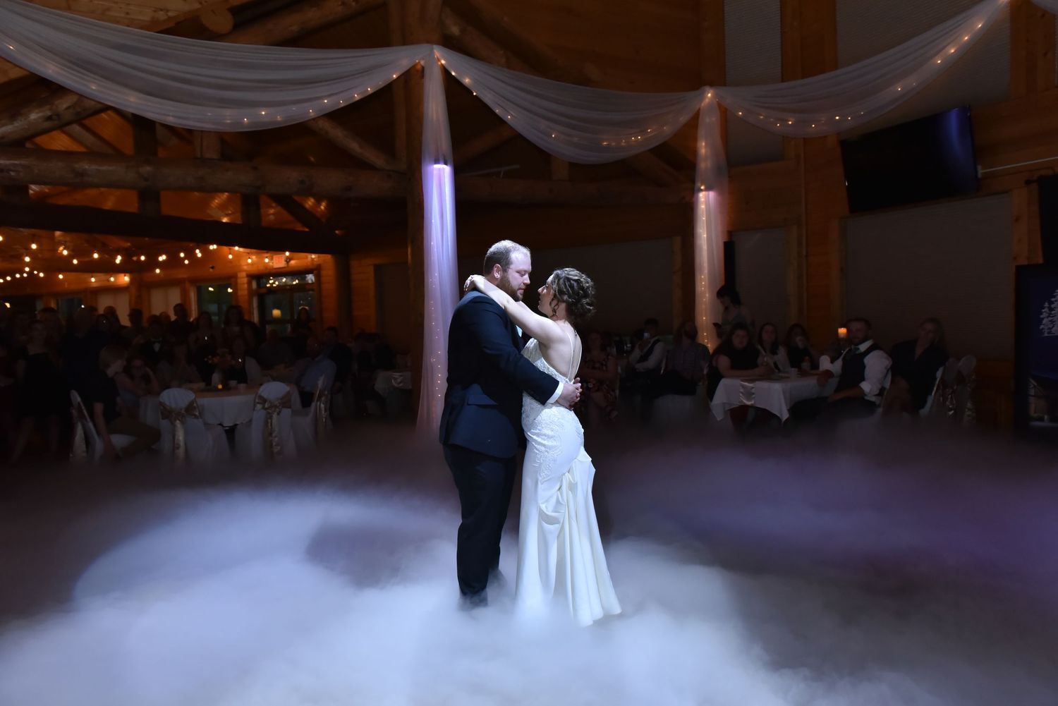 Newlyweds share their first dance in an elegantly lit reception hall with white draping and romantic ambiance.