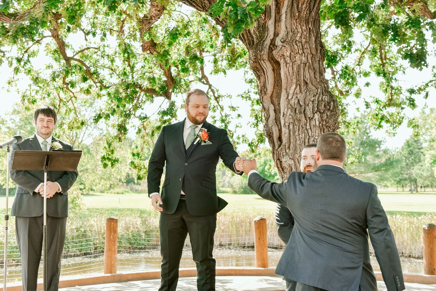 The Grands At Mulligans. A wedding ceremony takes place under a leafy tree on an outdoor wooden deck platform.