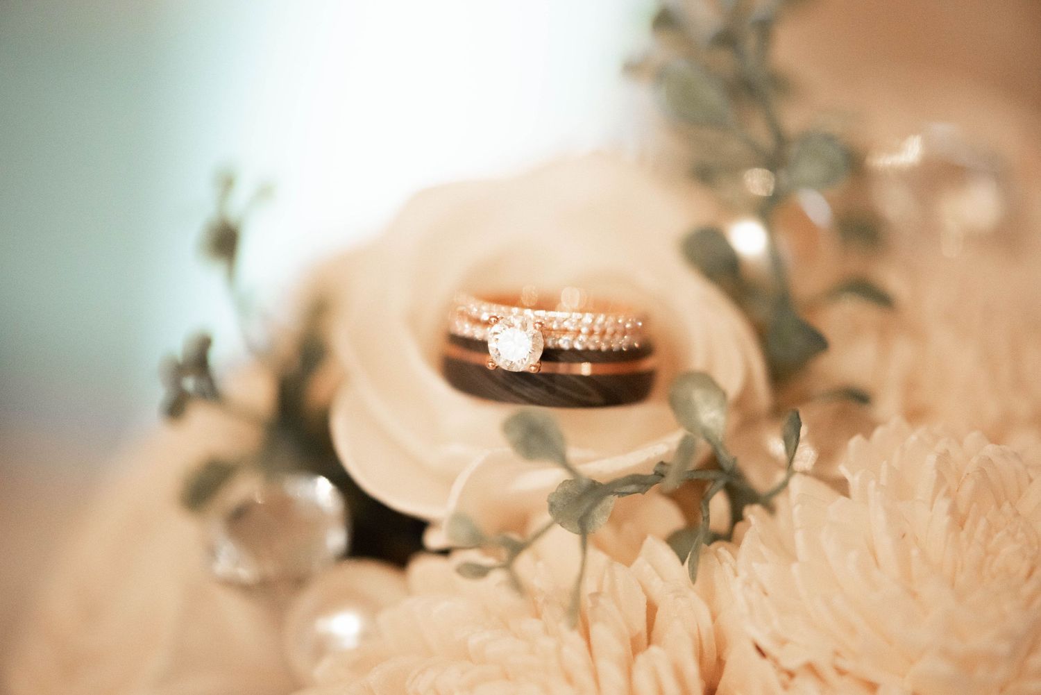 Gold wedding bands resting atop pale peach flowers with greenery accents.