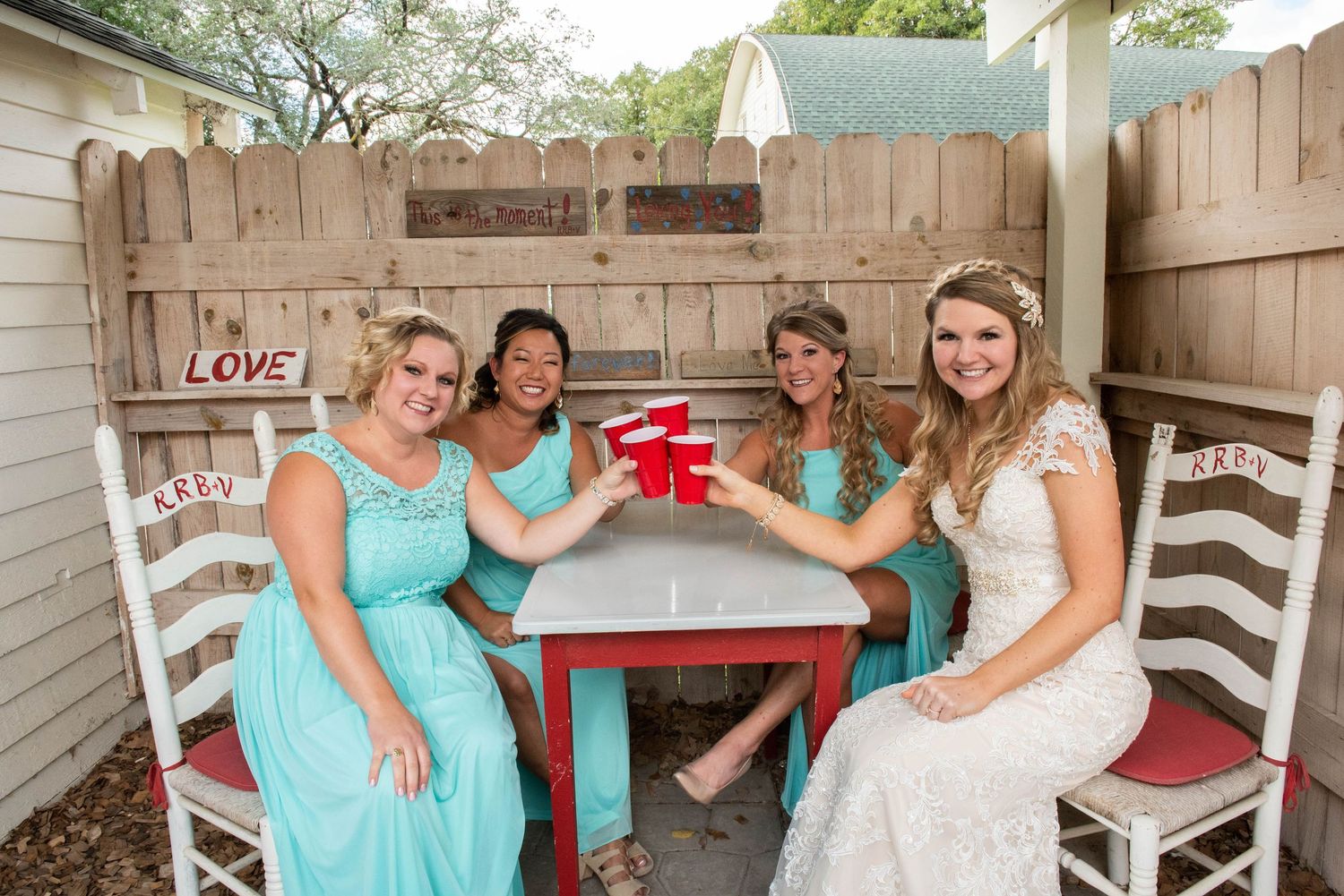 Bridal party in turquoise dresses toasting with red cups at an outdoor table. Rum River Barn Milaca Minnesota Weddings