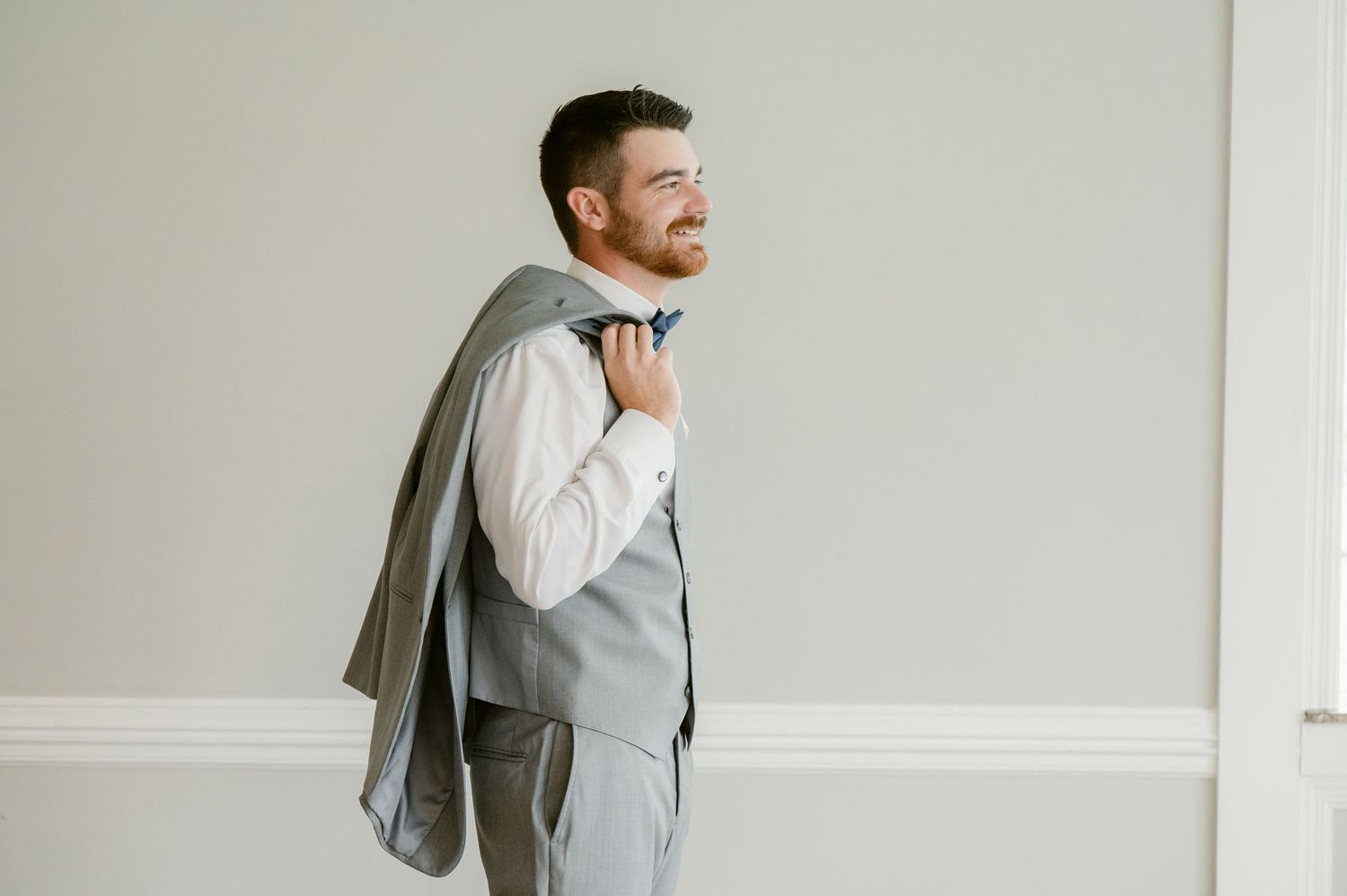 A casual wedding day portrait showing someone carrying their suit jacket over their shoulder.