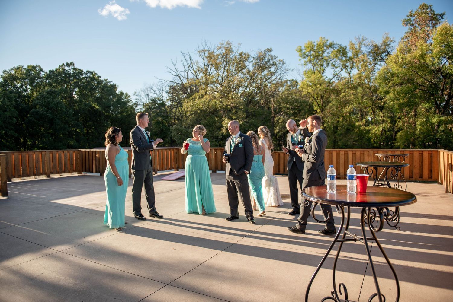 Wedding party guests gathered outdoors on a sunny patio with turquoise bridesmaid dresses. Rum River Barn Milaca Minnesota Weddings