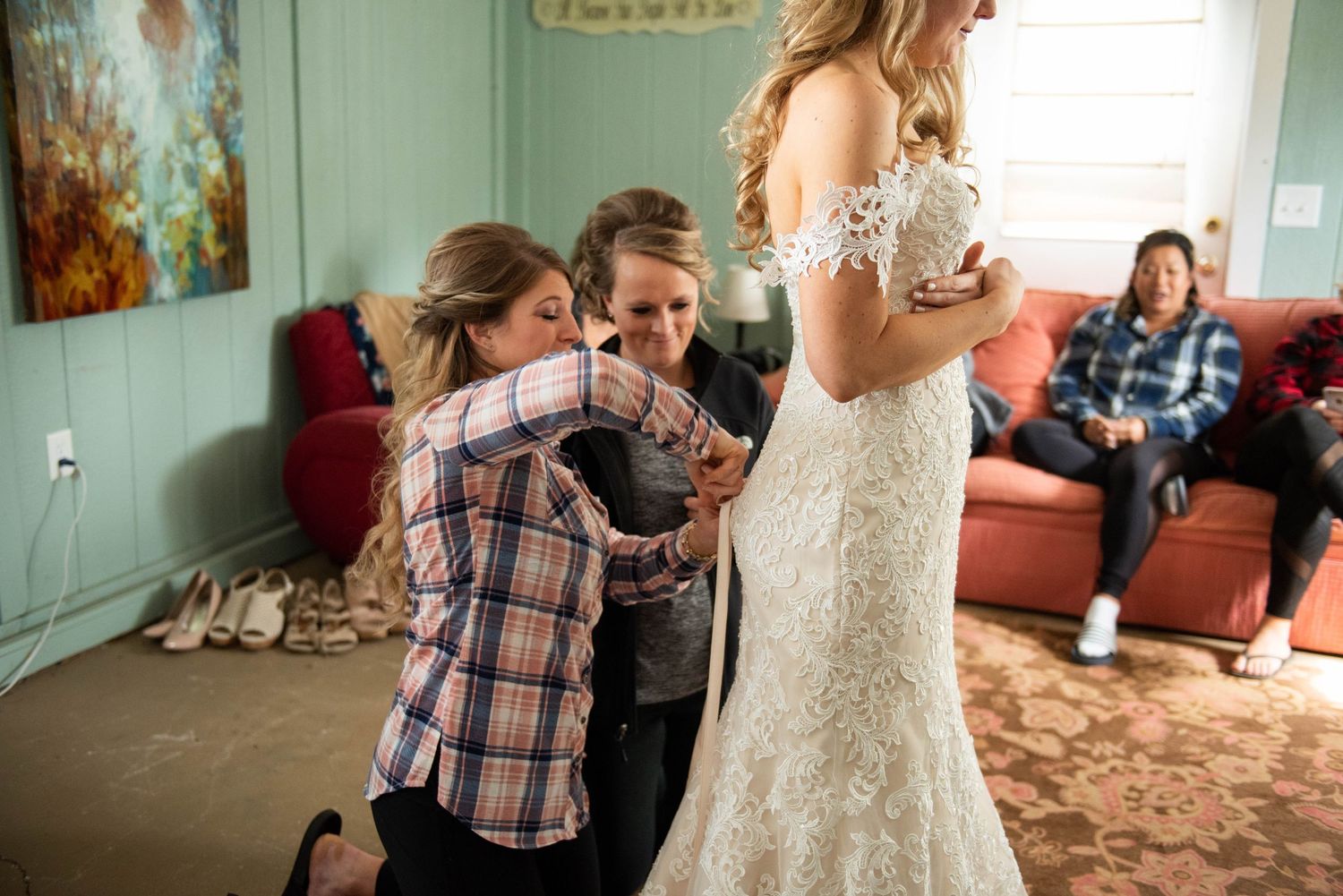 A touching moment during wedding preparations as guests help with the bride's elegant lace gown.