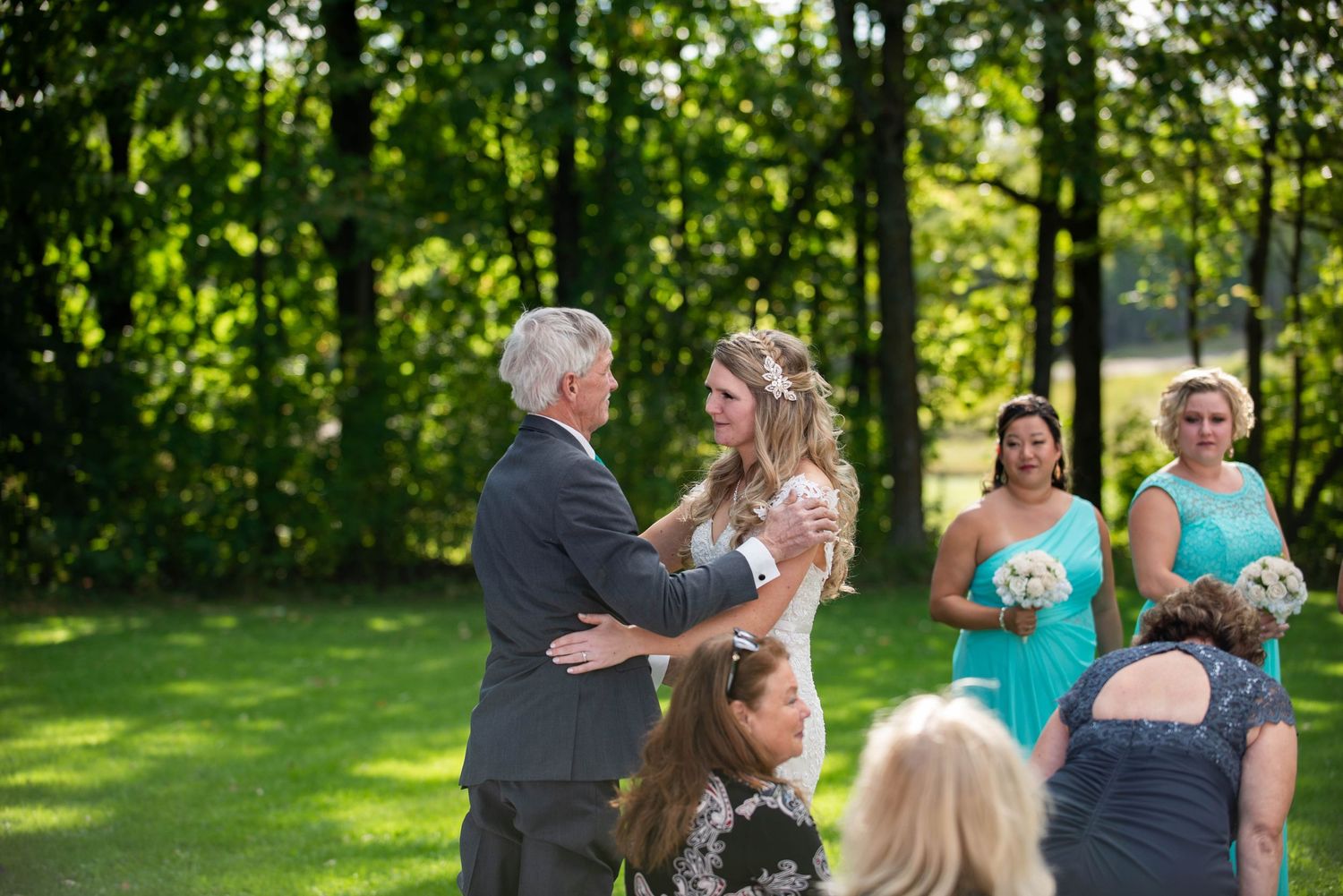 An outdoor wedding ceremony takes place on a sunny day with guests seated on a green lawn. Rum River Barn Milaca Minnesota Weddings