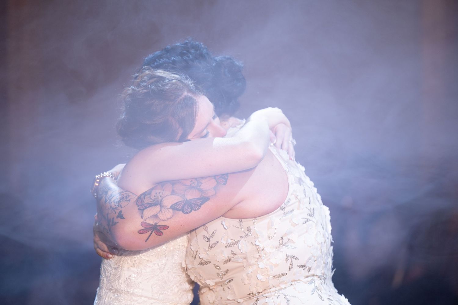 Couple embraces during emotional first dance under soft purple lighting.