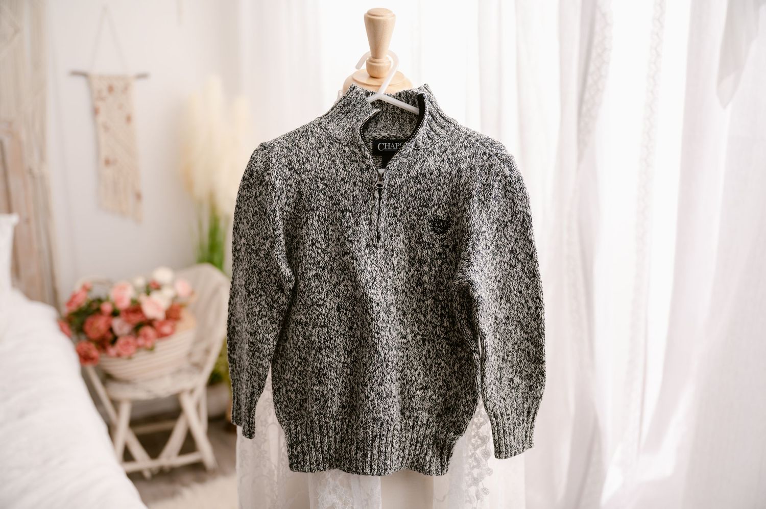 A grey marled half-zip knit sweater displayed on a wooden mannequin bust near soft curtains and pink flowers.