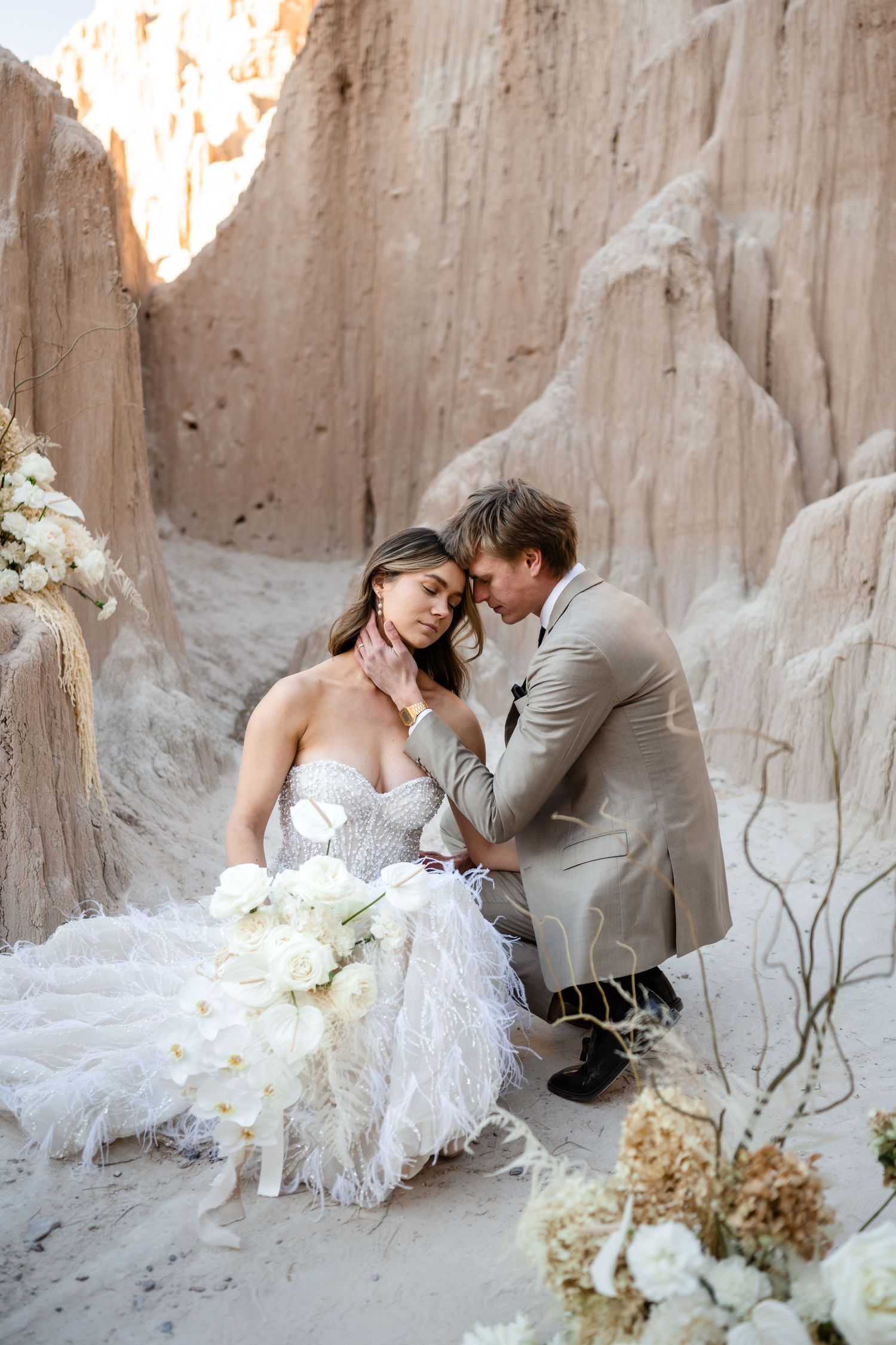 A romantic wedding couple shares an intimate moment in a sandy canyon with white floral decorations.