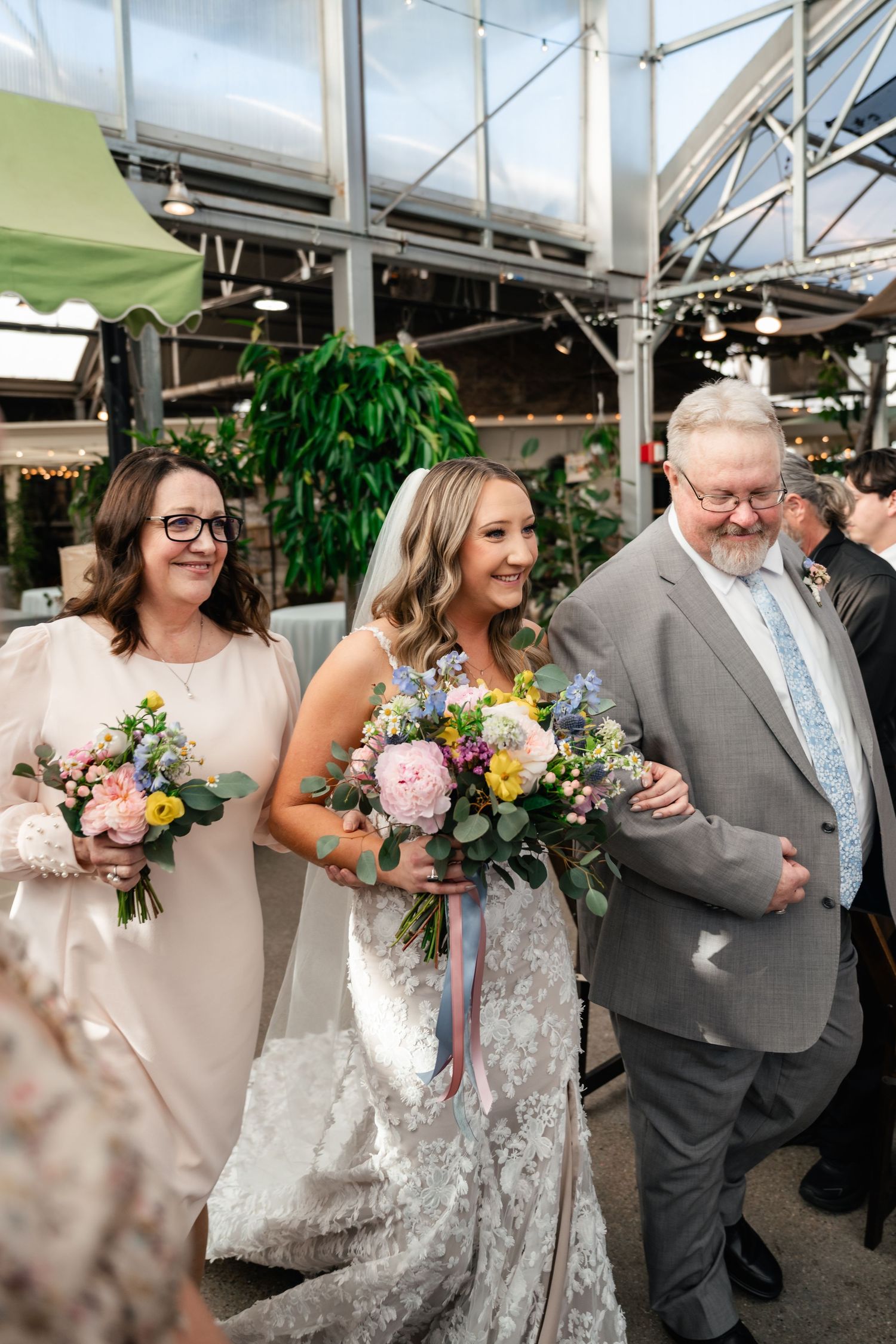 Wedding celebration at a greenhouse venue with elegant floral bouquets featuring pink and yellow blooms.