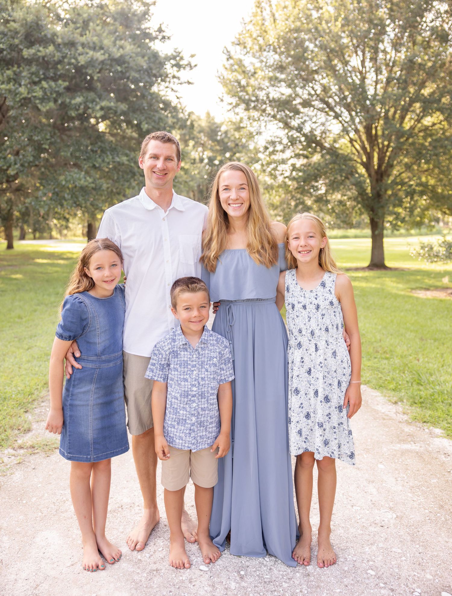 A family stands together outdoors on a path during golden hour with trees in the background.