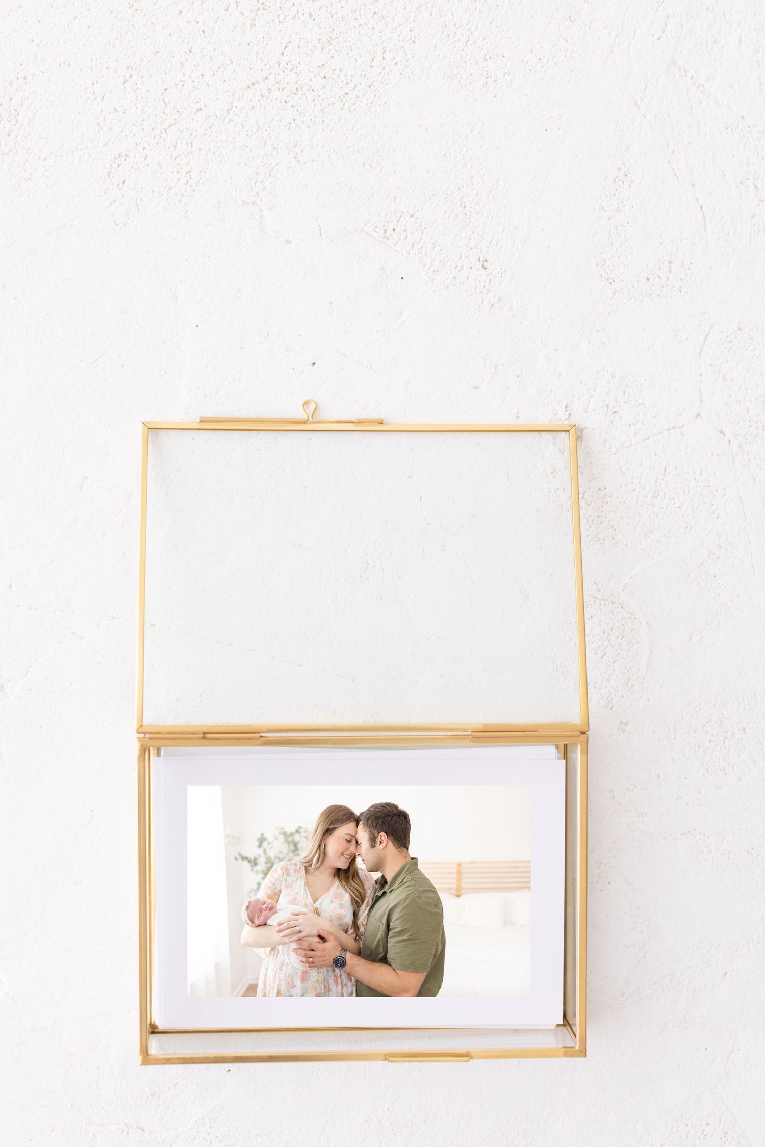A decorative gold glass display box holds a romantic photograph against a white textured wall.