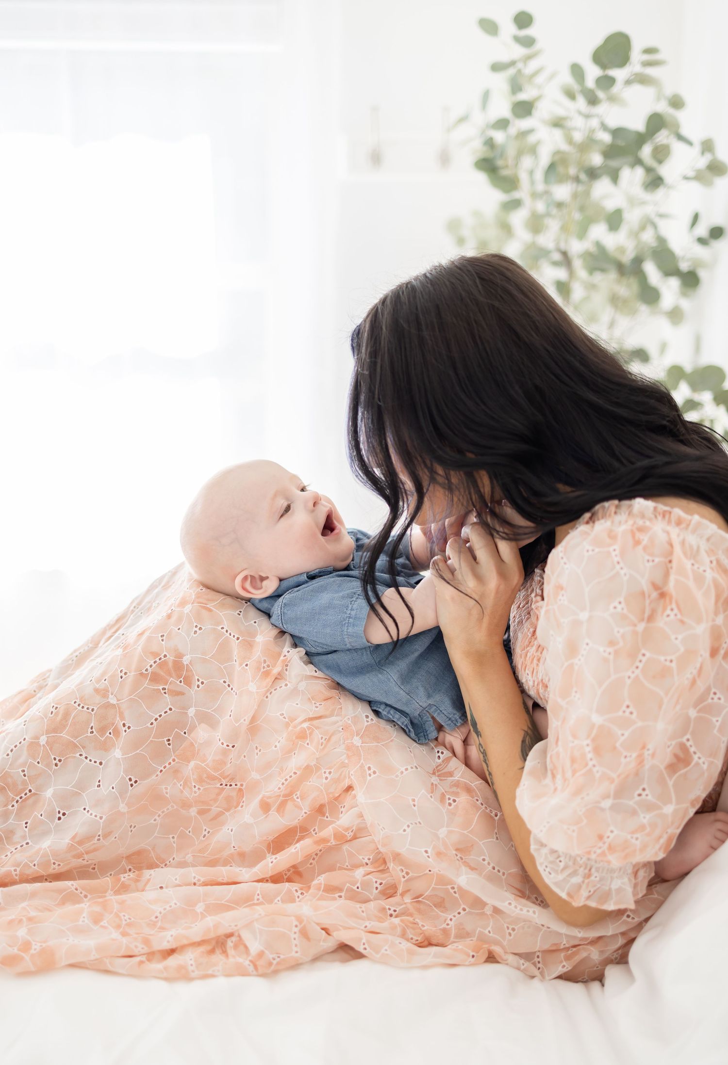 A tender moment between parent and baby as they lie together in peaceful serenity, dressed in peach lace and blue.