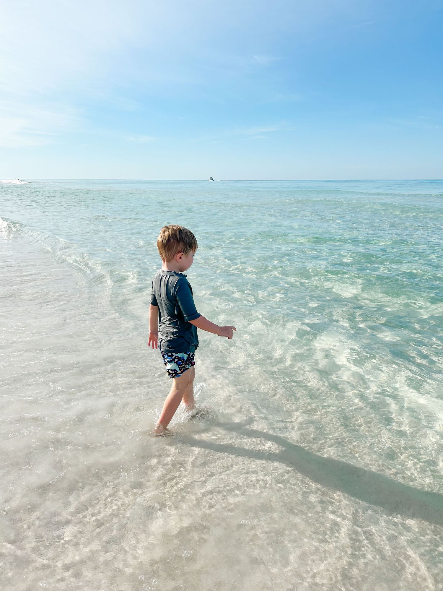 Small figure in swim clothes stands in clear turquoise water at the edge of a pristine white sand beach.