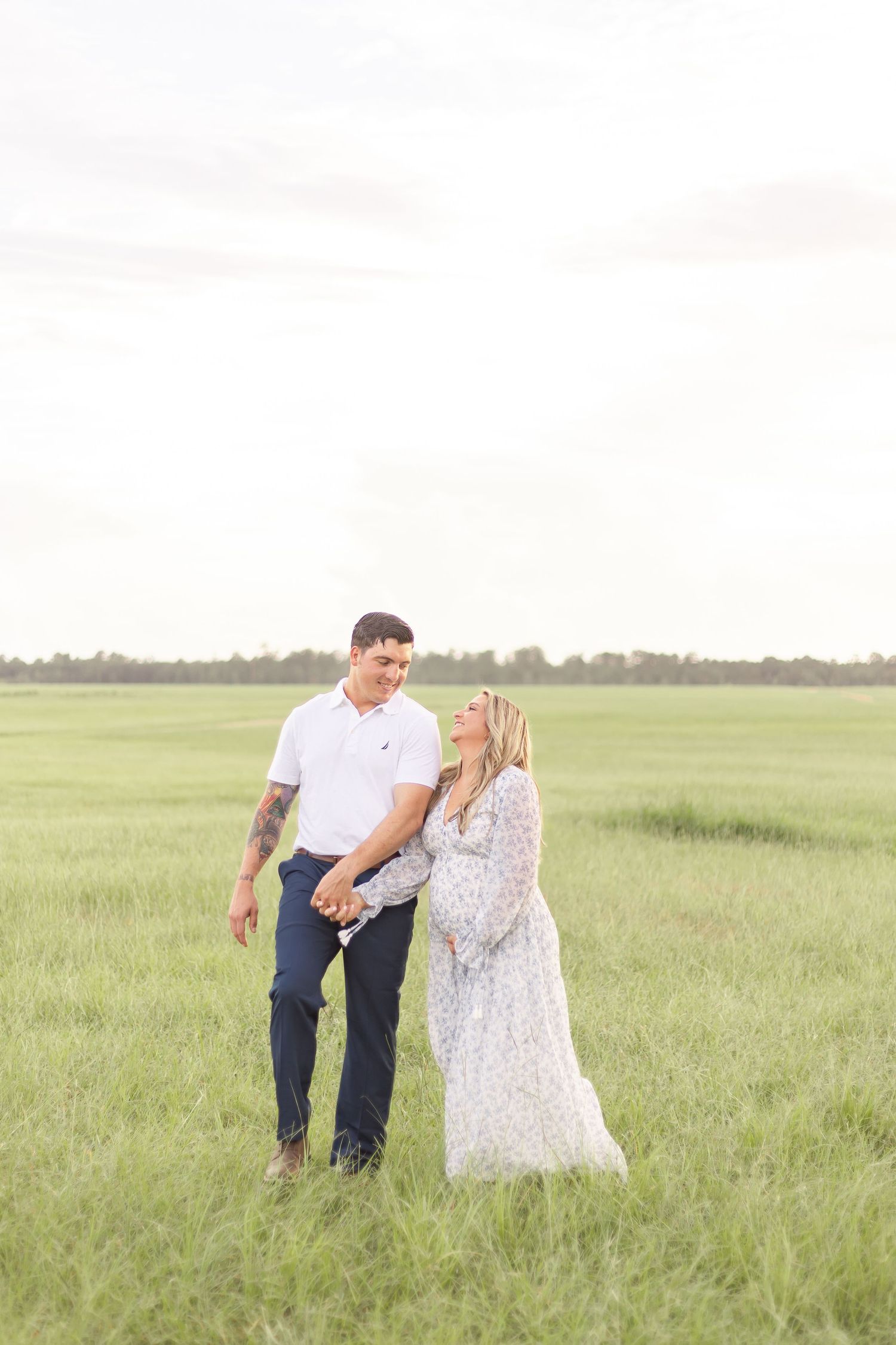 A couple shares a joyful moment together in a serene green field during golden hour.
