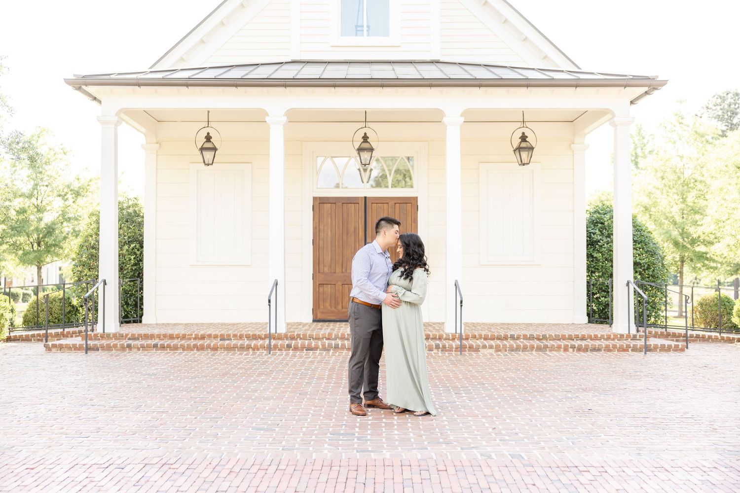 A romantic moment shared on a brick patio in front of a white chapel with hanging lanterns and wooden doors.
