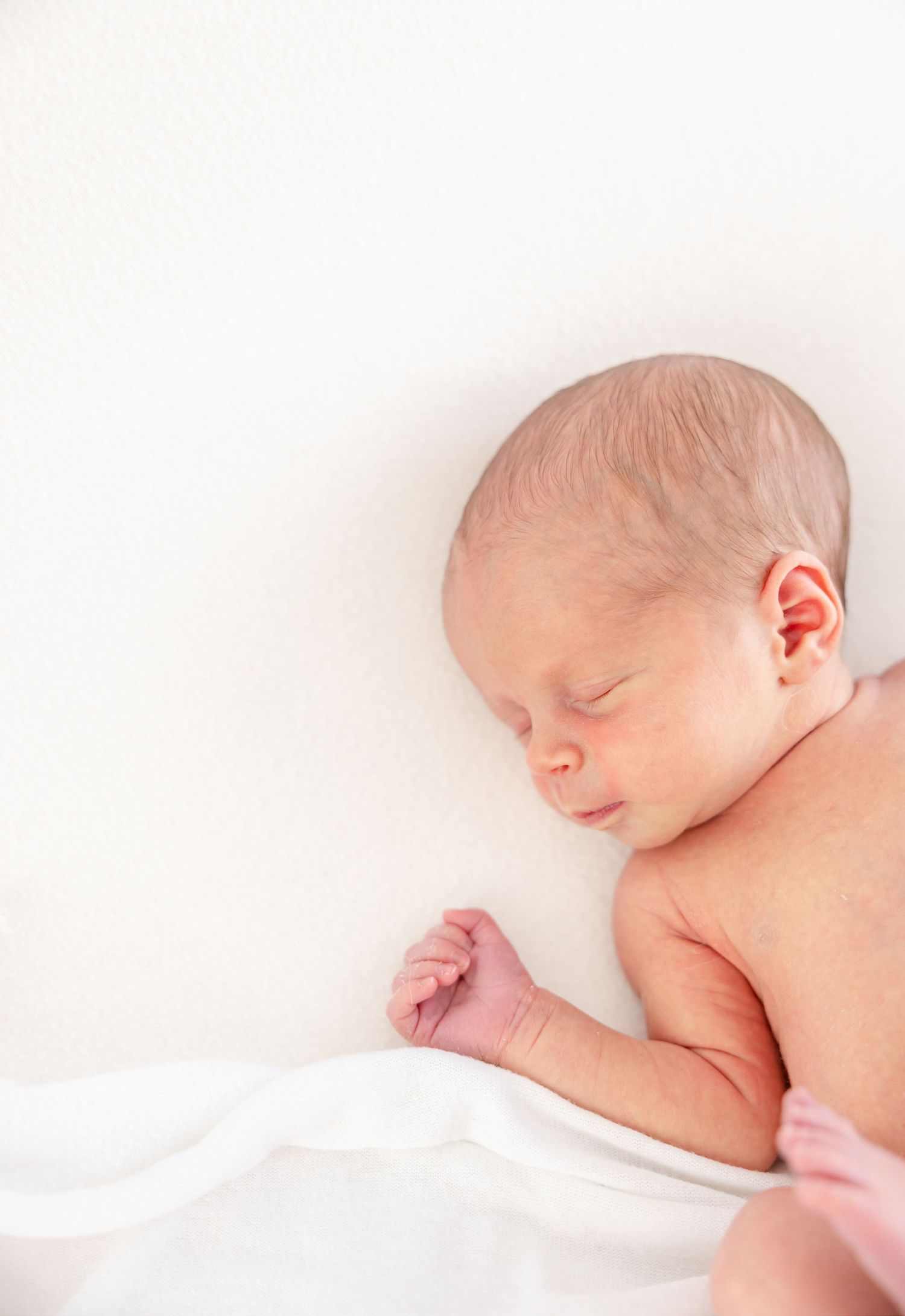 A peaceful sleeping newborn baby rests on soft white bedding in a minimalist photography setting.
