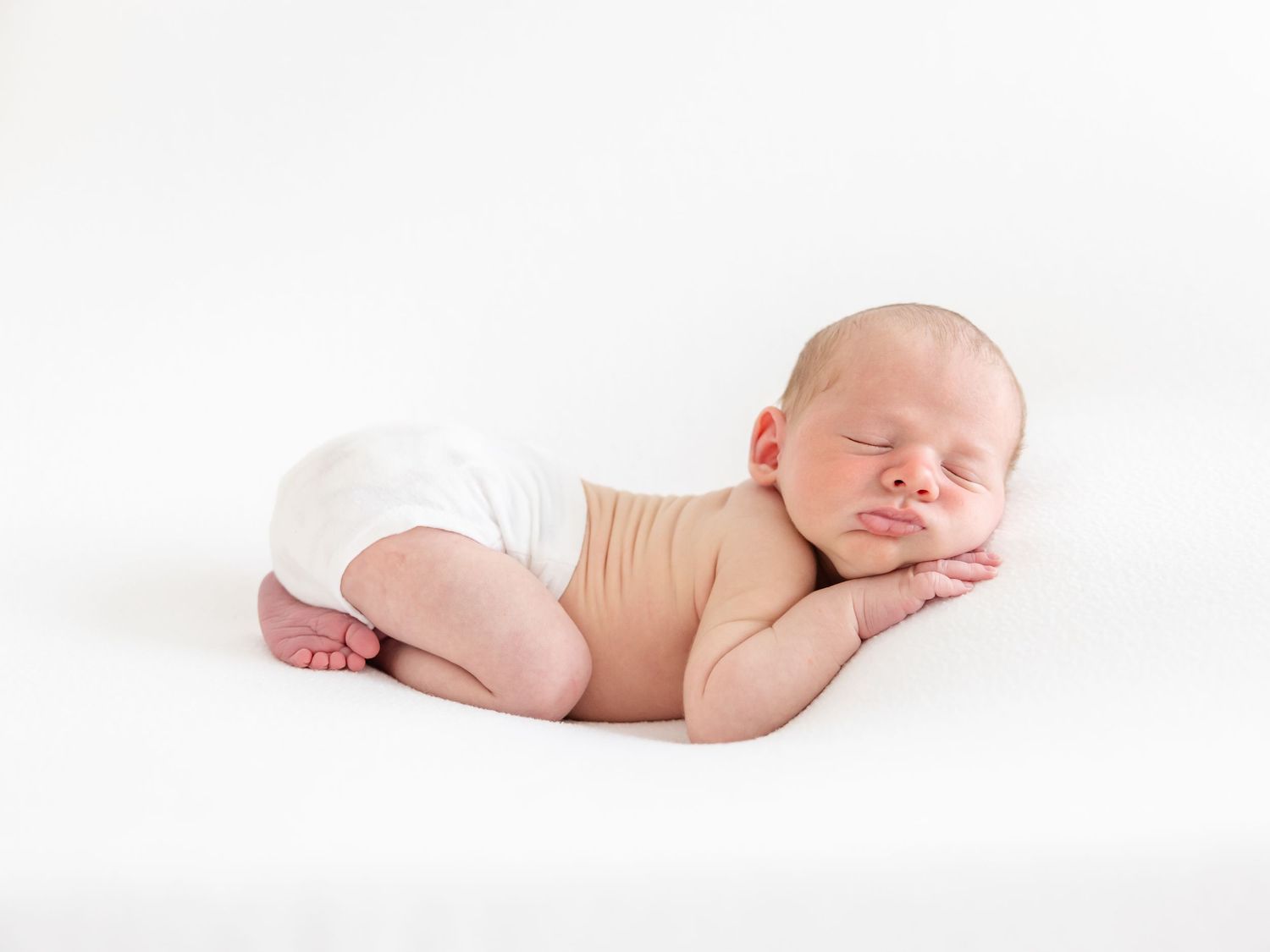 Sleeping newborn laying on a white blanket at his Columbus, GA Newborn Portrait session.