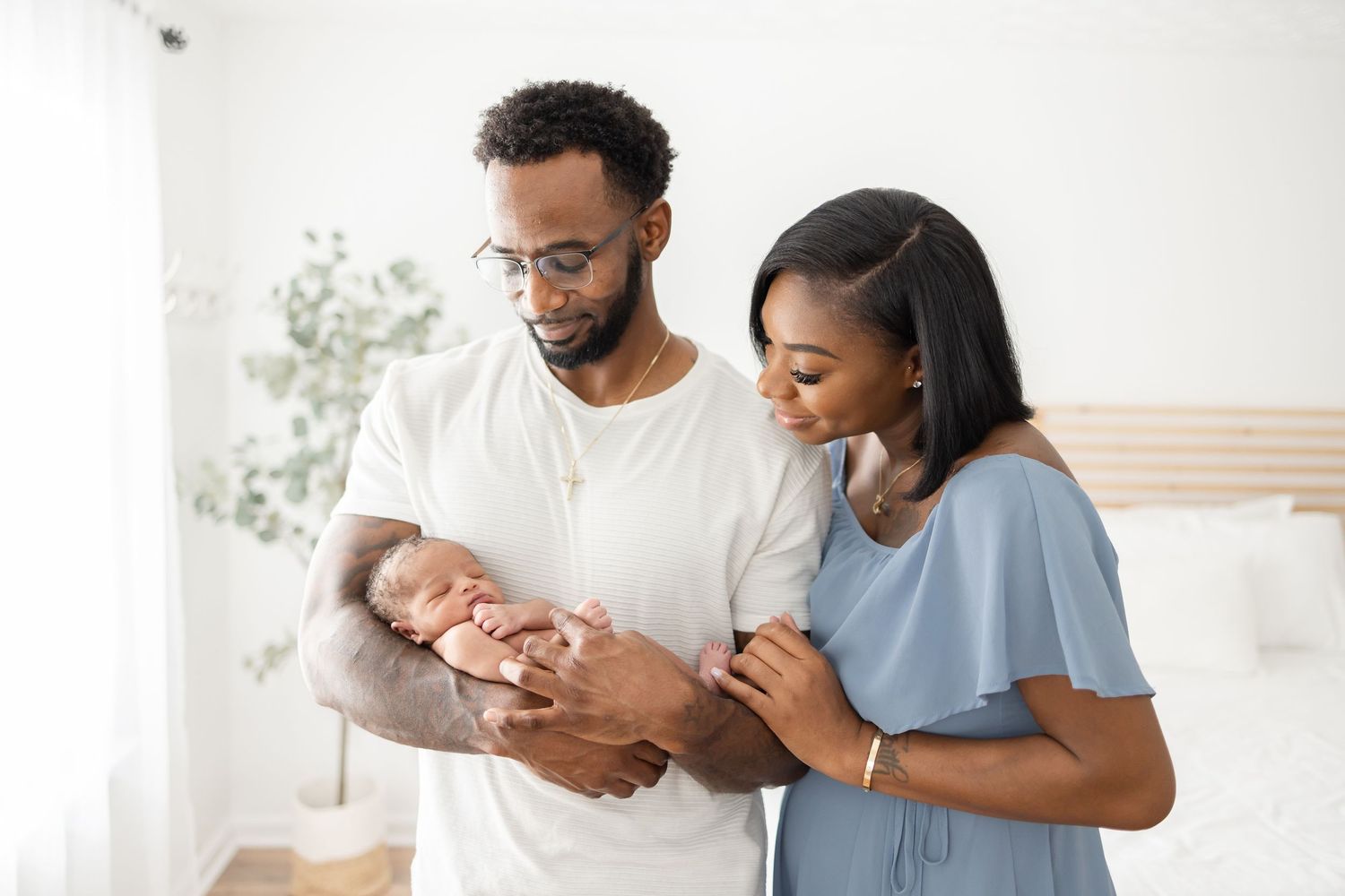 Happy couple in casual attire tenderly holding and gazing at their newborn baby in bright bedroom setting.