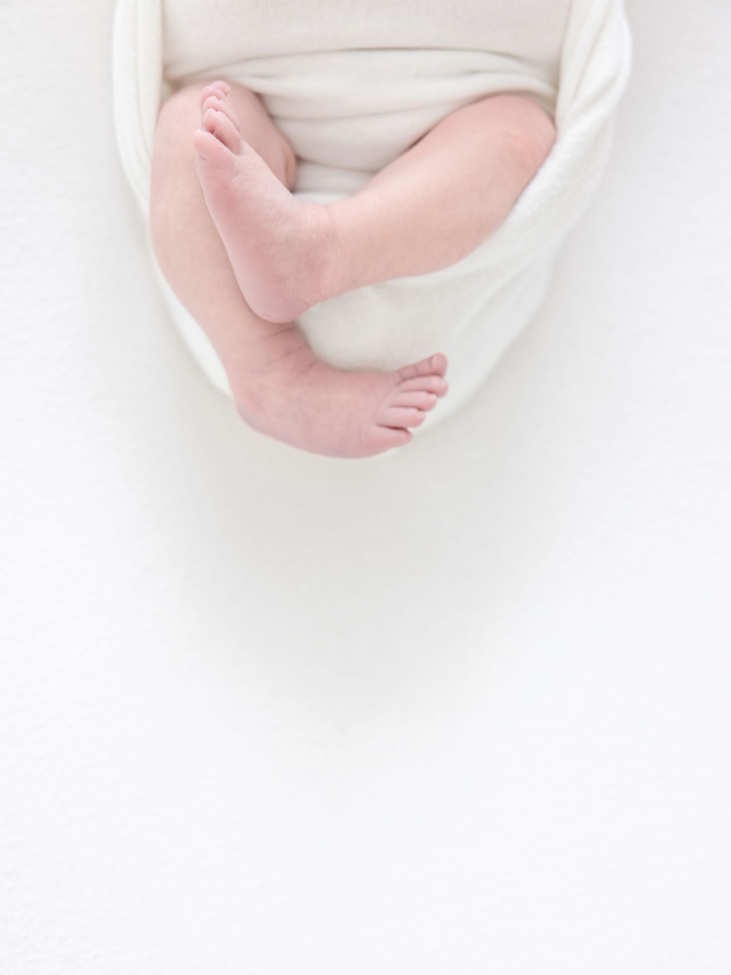 Baby feet resting on soft white fabric shown in a delicate close-up photograph taken by a Columbus, GA newborn photographer.