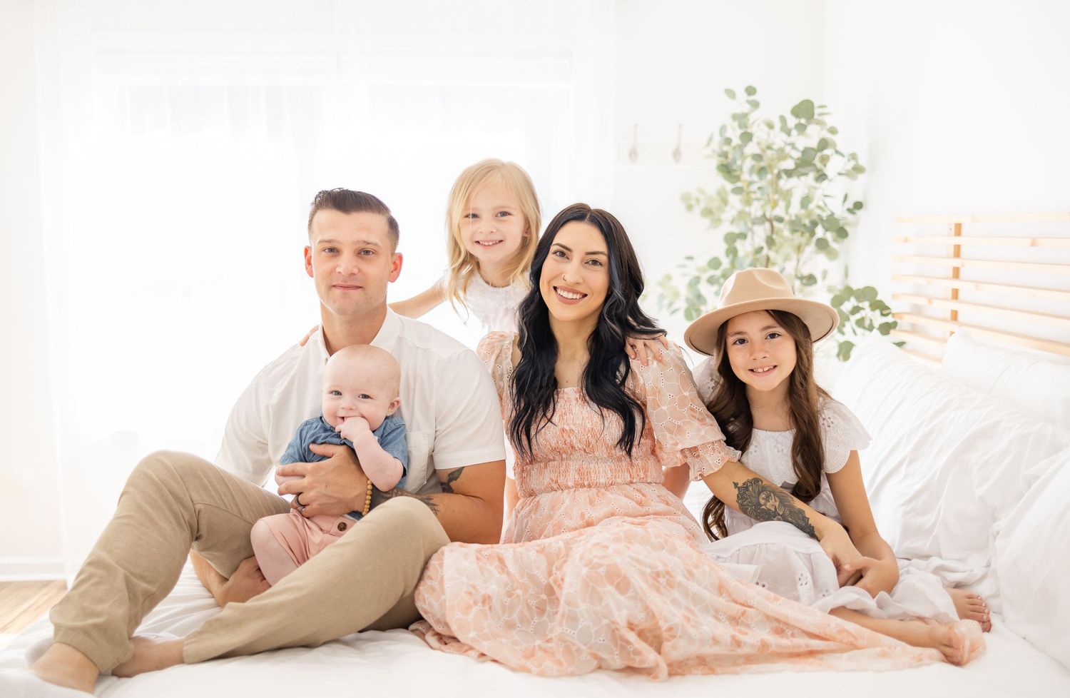 A family in coordinated light-colored outfits sits together on a white couch with elegant decor.