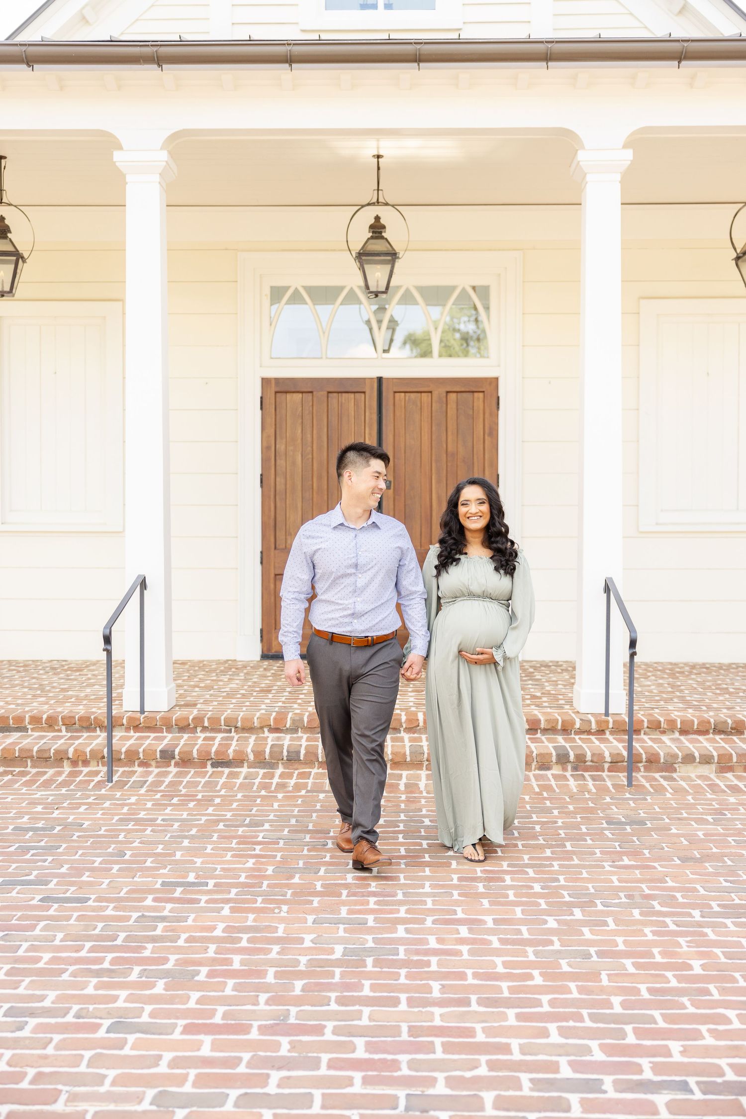 A couple stands lovingly together on a brick patio in front of an elegant southern-style porch entrance with white columns.