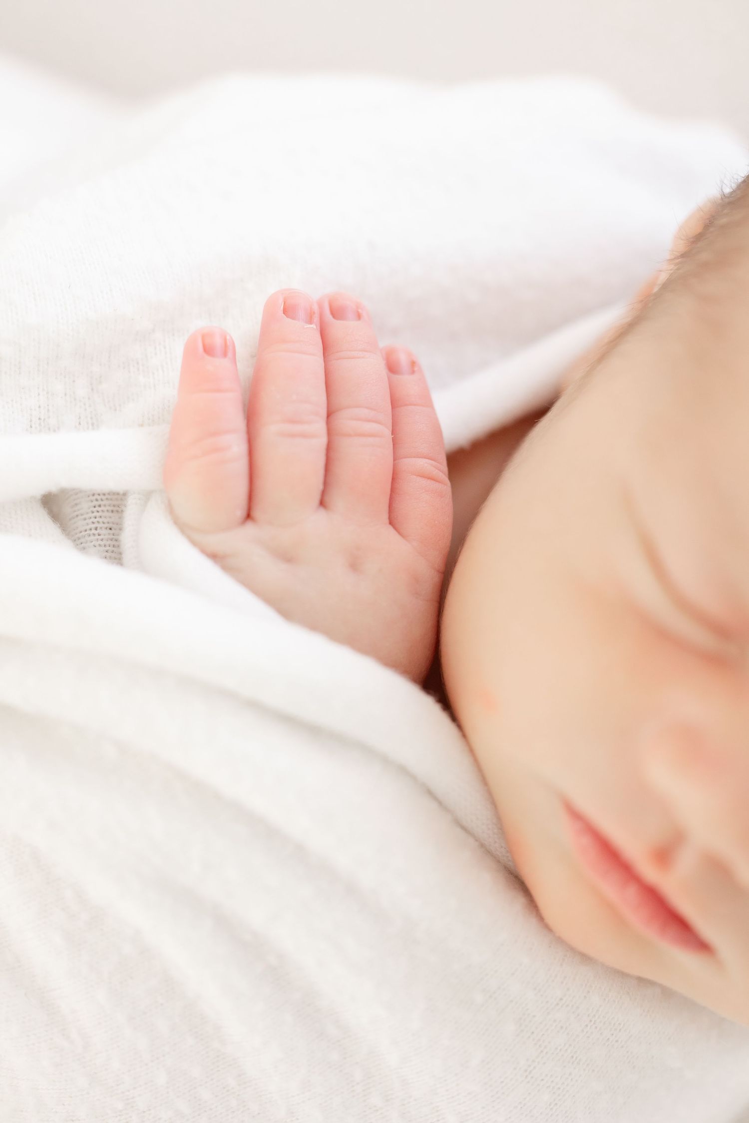 Close up of a sleeping baby's tiny hand against soft white blankets during peaceful naptime.