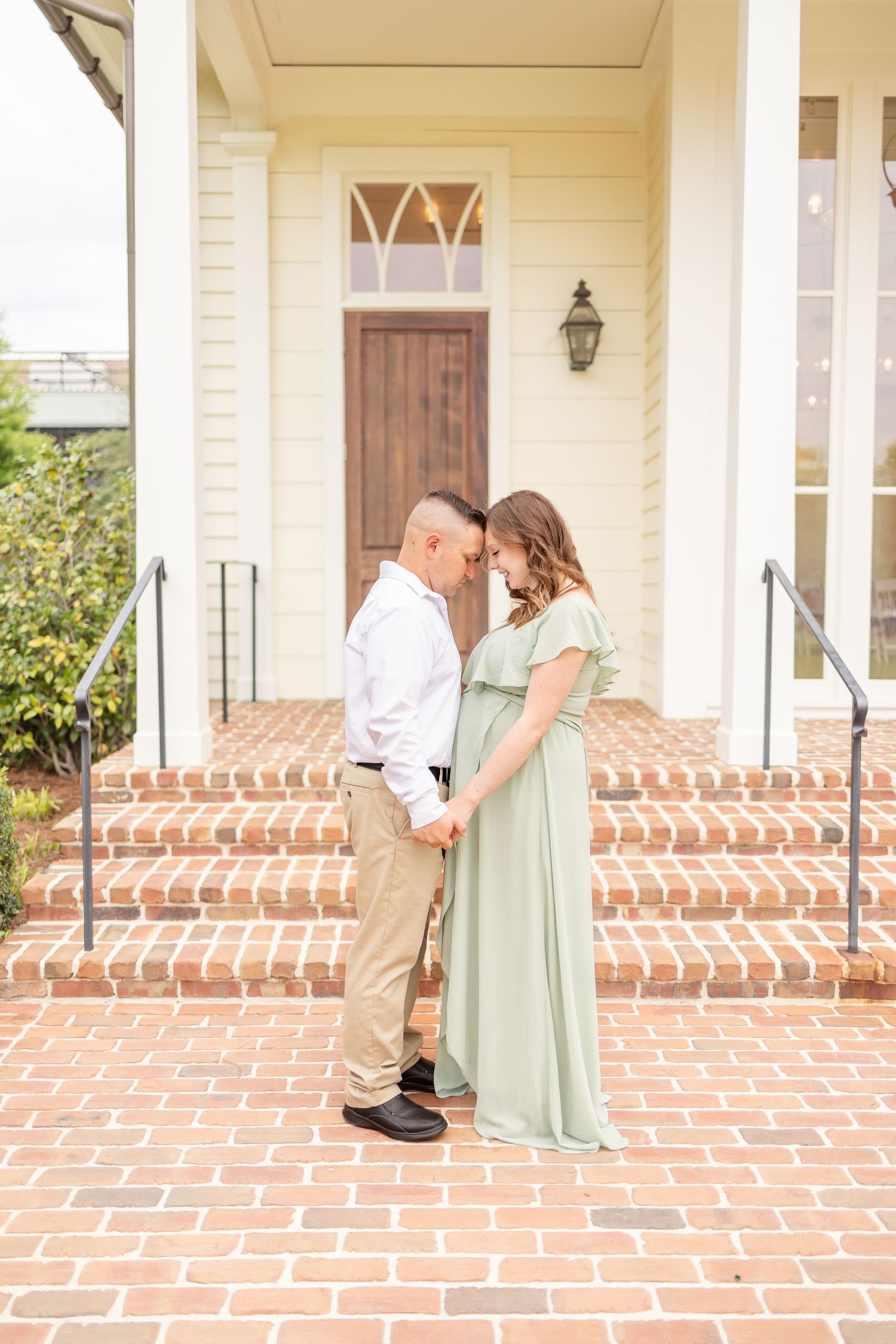 A romantic couple shares a tender moment on brick steps in front of a traditional home with elegant cream siding.