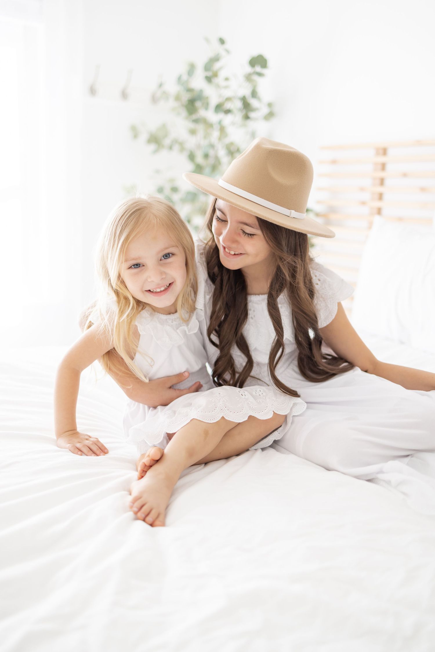 White boho aesthetic photo of two people wearing lace dresses sitting together on white bedding.