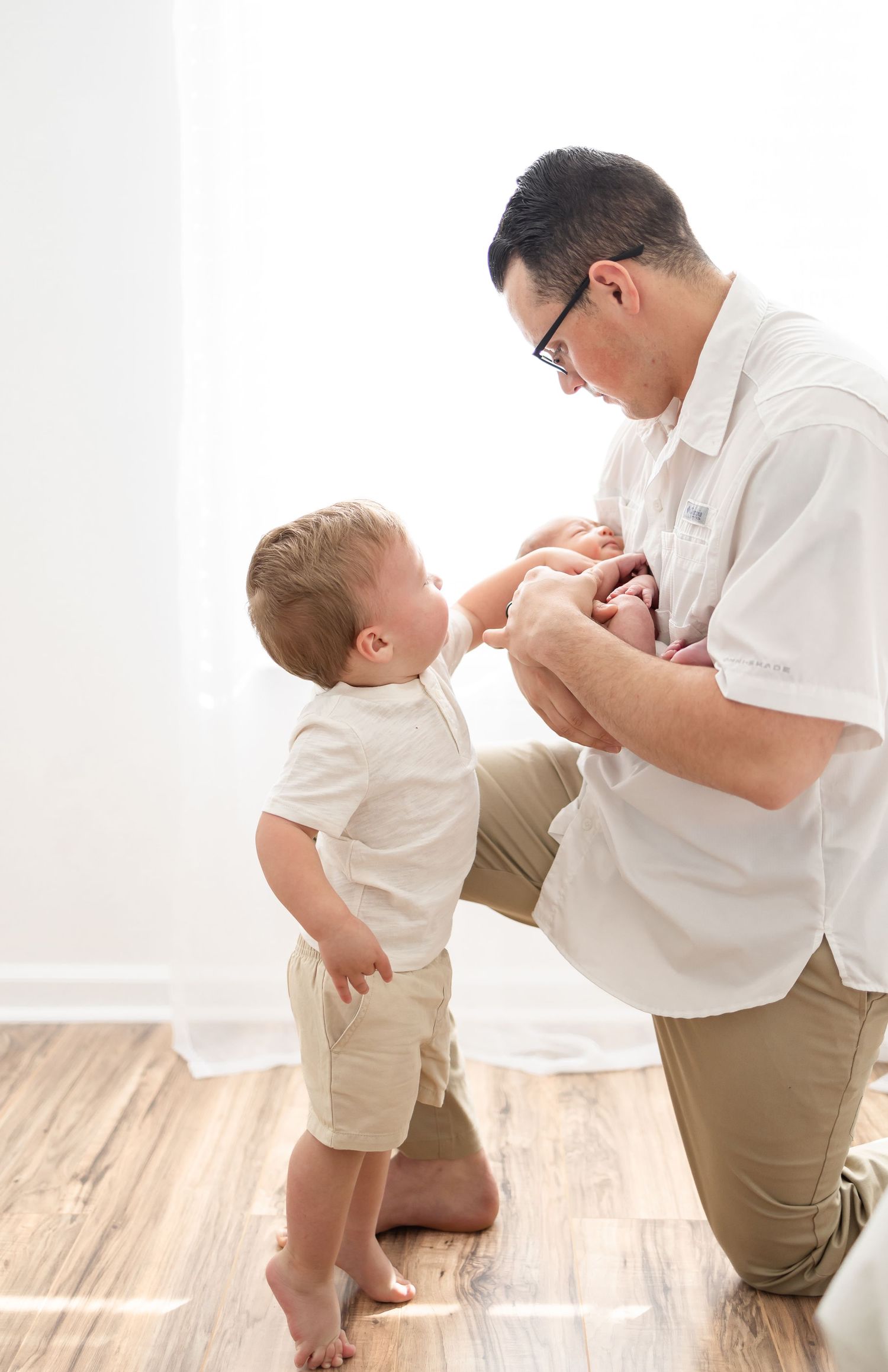 Sweet indoor portrait of parent and two children wearing matching white shirts and khaki bottoms on hardwood floor.