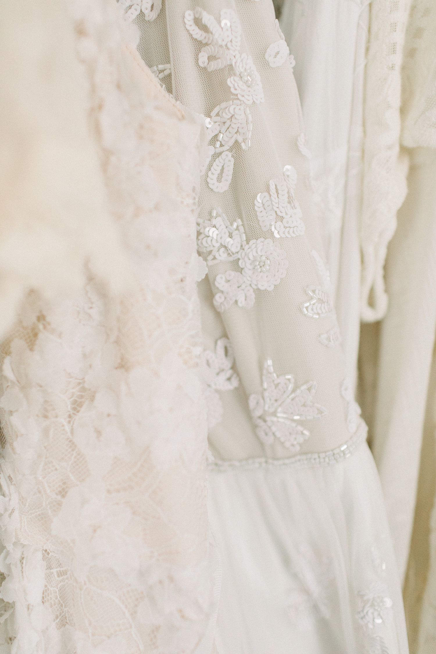 Close-up detail of delicate white lace and embroidered floral patterns on a wedding dress fabric.