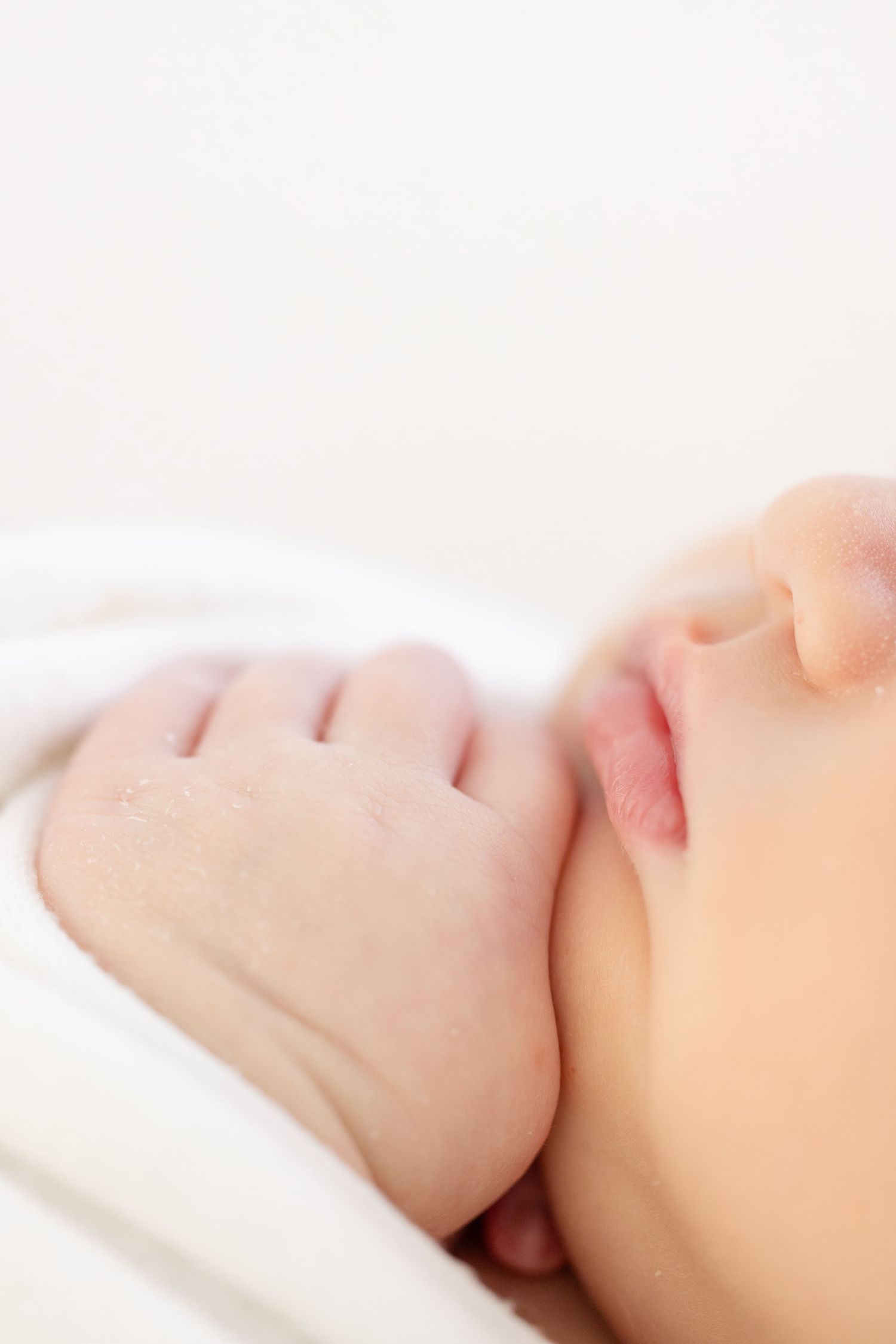 A sleeping baby rests peacefully on white bedding in a close-up shot focused on their soft features.
