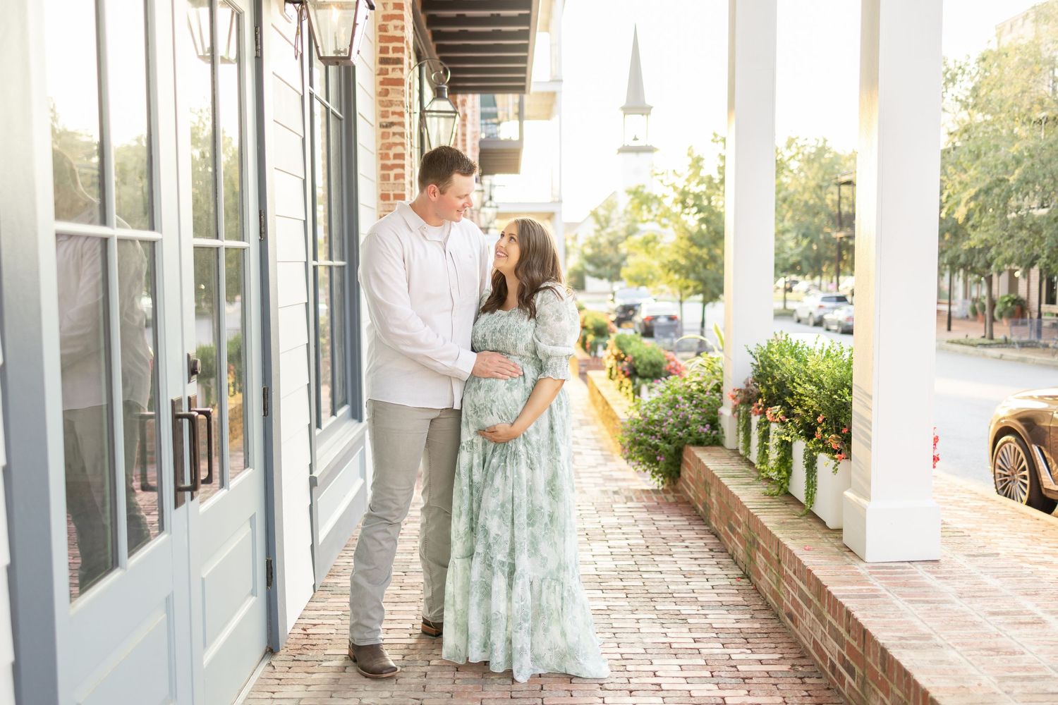 Two people in coordinated outfits share a sweet moment on a quaint southern porch with white columns and brick details.