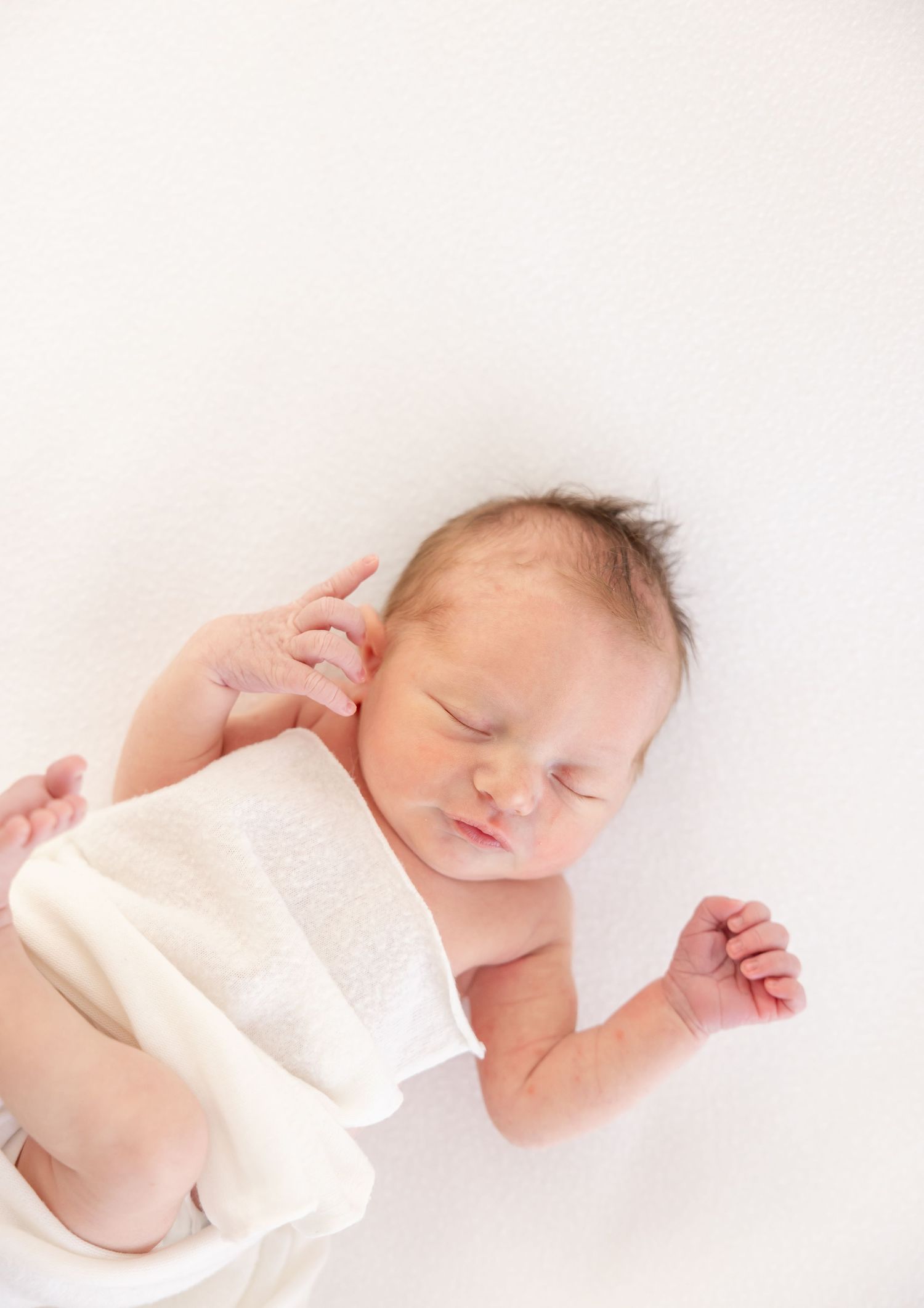Sleeping newborn baby wrapped in soft white blanket against light background.