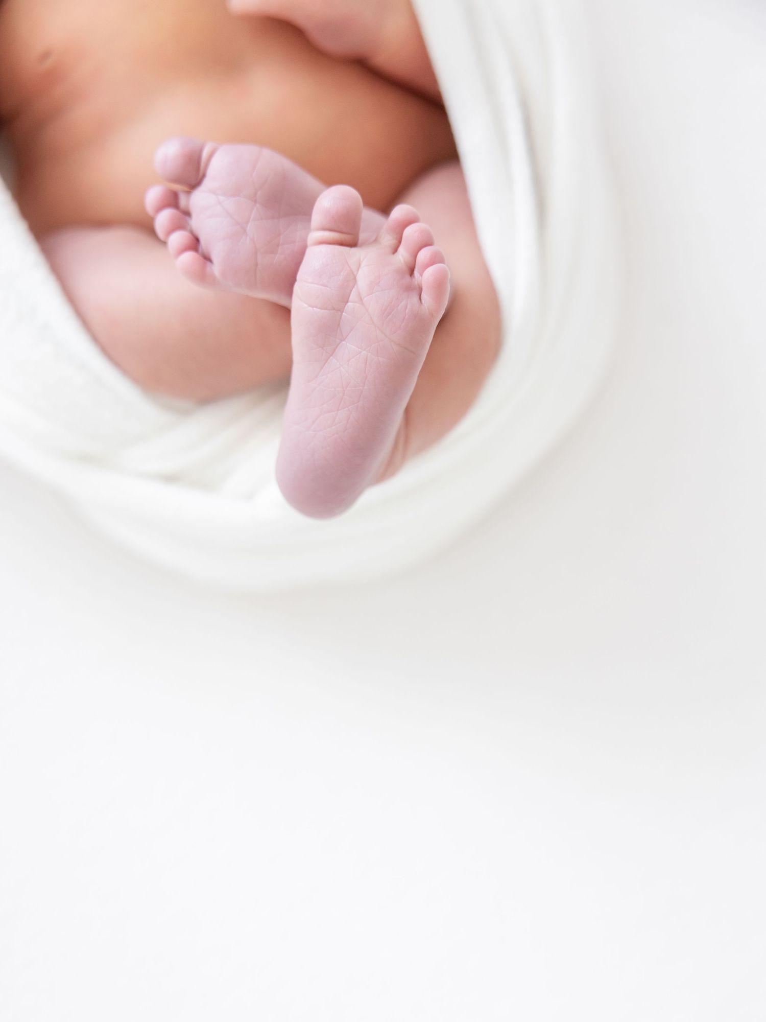 Tiny newborn baby feet wrapped in soft white blanket with gentle lighting.
