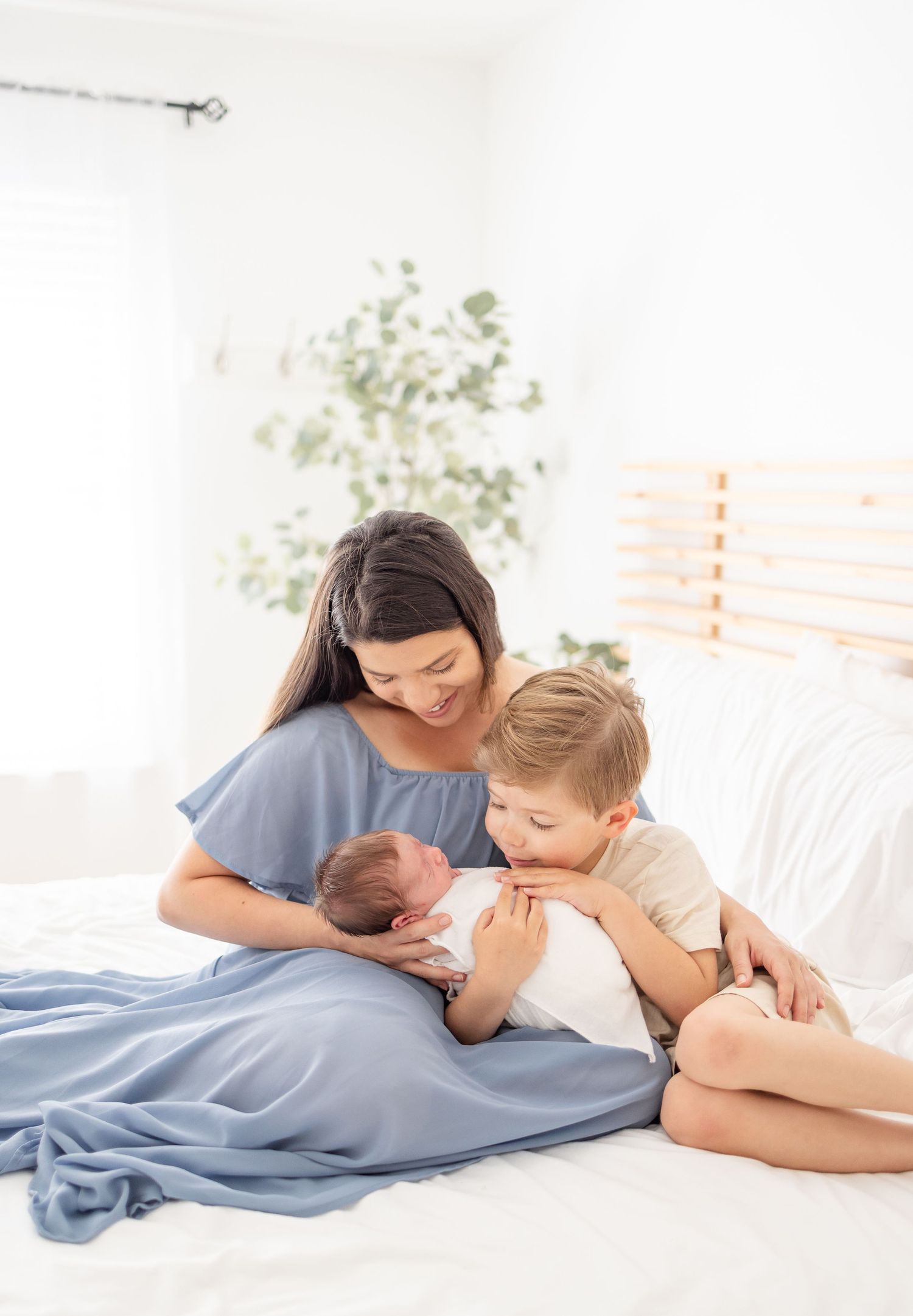 A tender family moment on a white bed with blue bedding as they cuddle with a newborn baby.